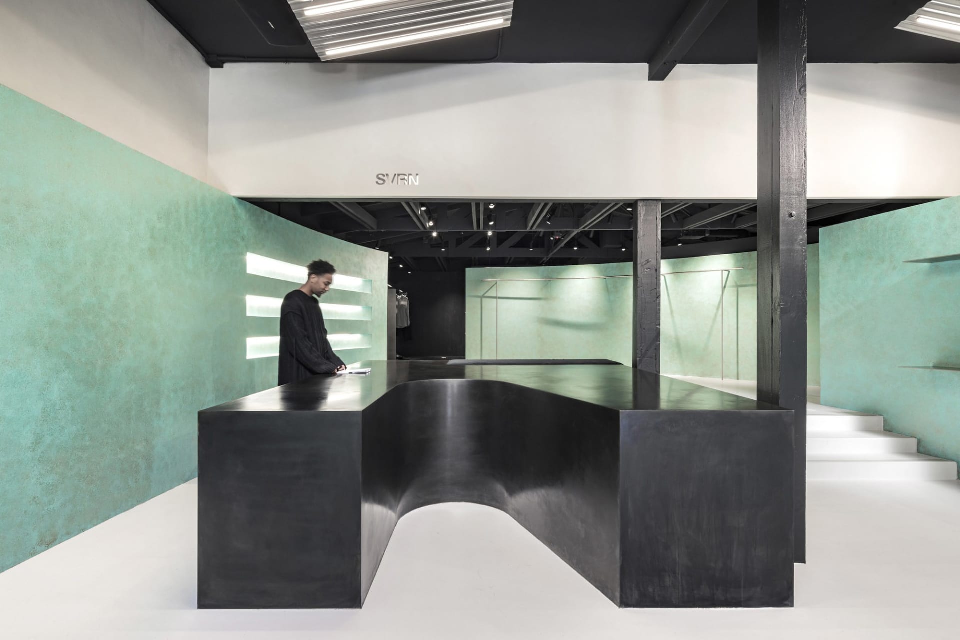 A modern retail storefront with a sleek black curved reception desk, turquoise walls, and white flooring.