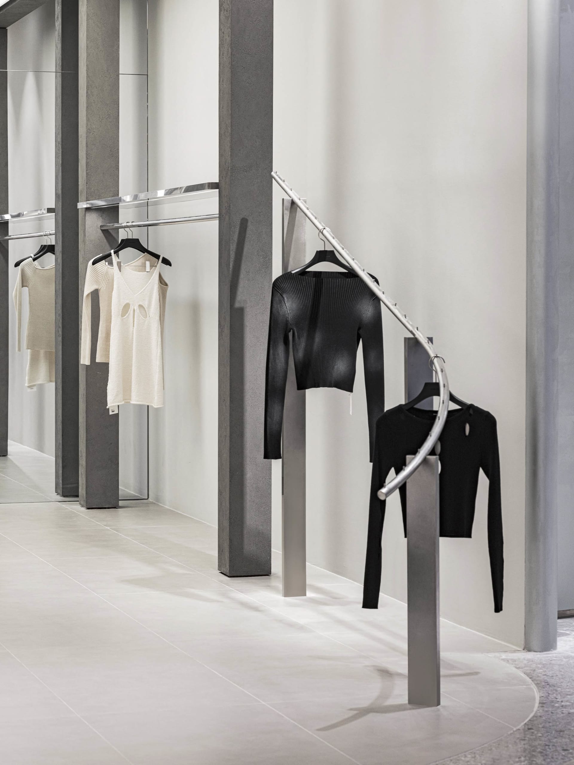 一家現代零售服裝店以金屬衣架展示極簡服裝,搭配混凝土與玻璃的室內設計。