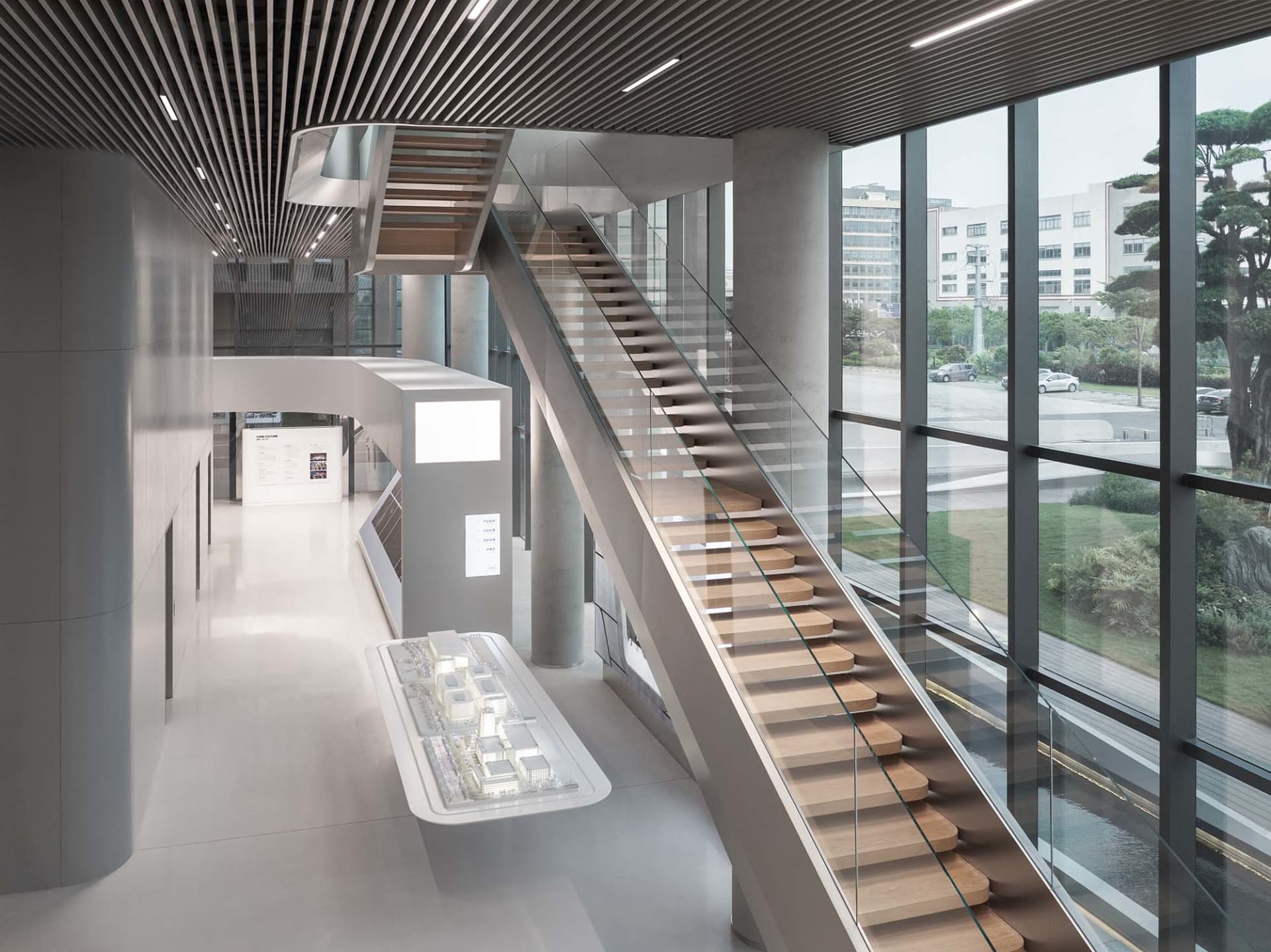 A modern office space featuring glass and steel construction with a large staircase and a view of the exterior through large