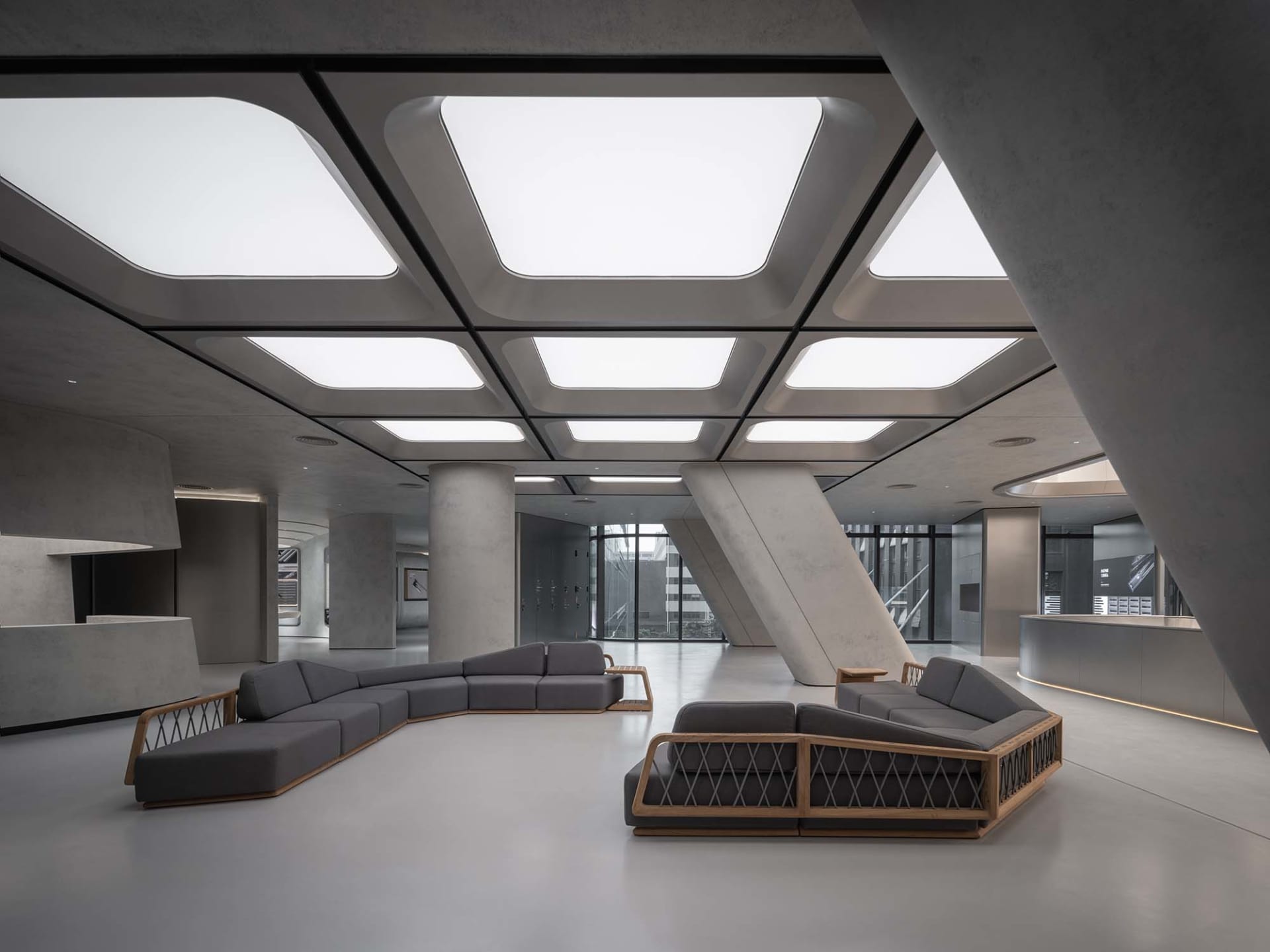 Modern minimalist office lobby with concrete walls and floors, featuring sleek furniture and large skylights.