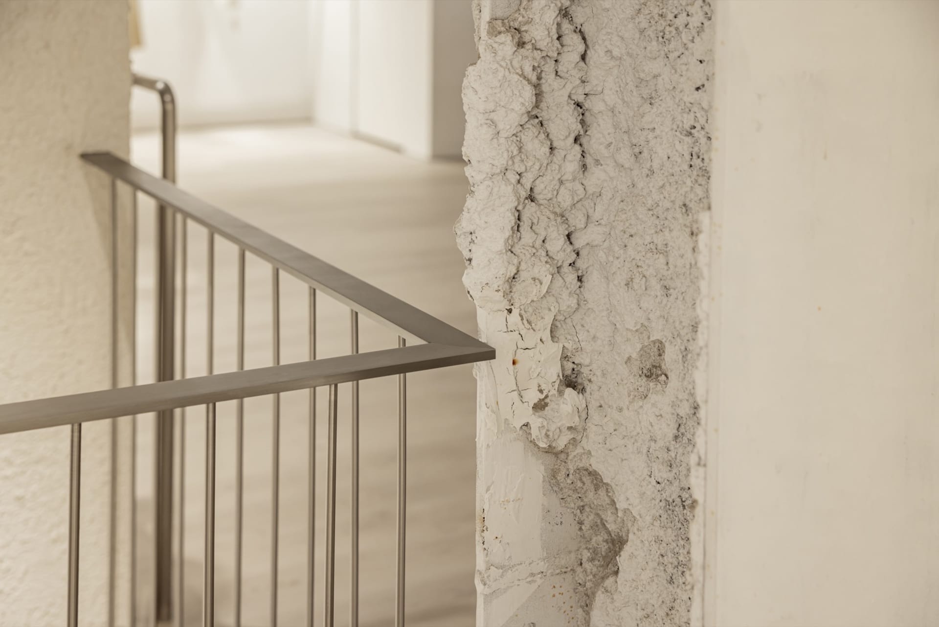 A close-up view of a stairway with a concrete wall featuring a textured, cracked surface and a metal railing.