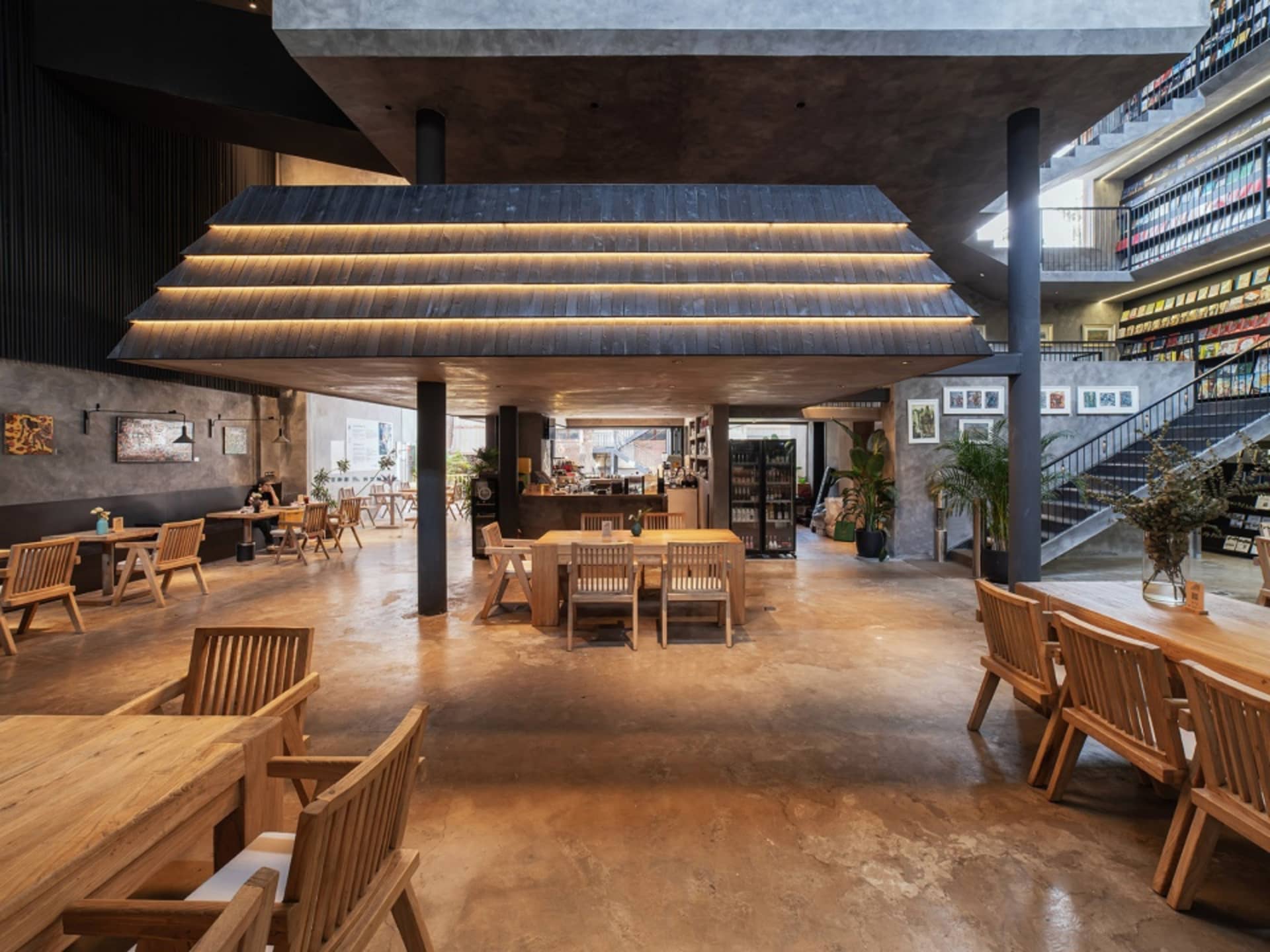 Well-lit industrial-style café interior with concrete flooring, wooden furniture, and bookshelves.