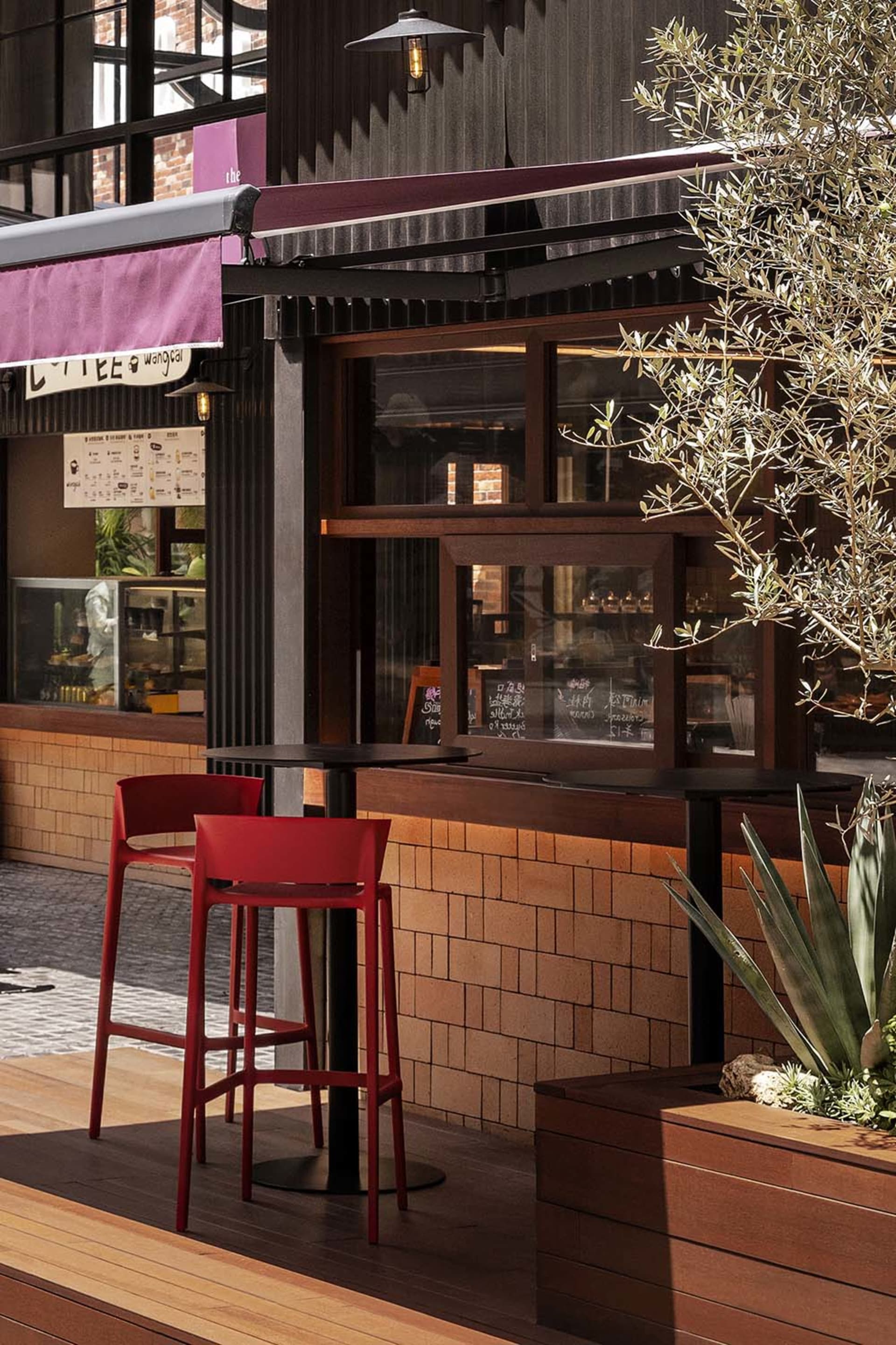 An industrial-style cafe interior with wood accents, high stools, and potted plants.