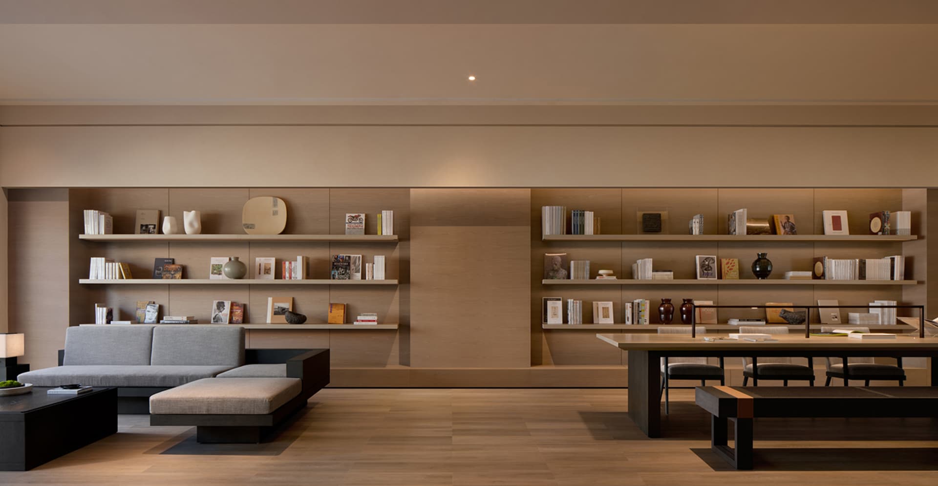 A modern library with wooden shelves containing books and decorative items. The floor is wooden, and there is a large sofa in