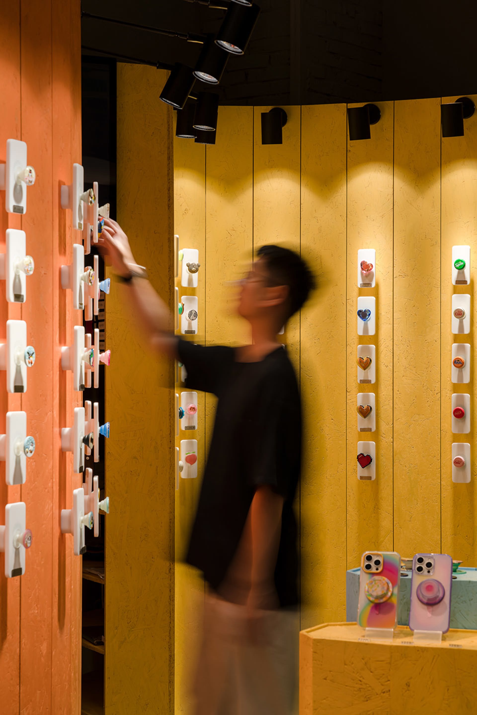 一位顧客在零售店內與色彩繽紛的手機握把配件展示互動。