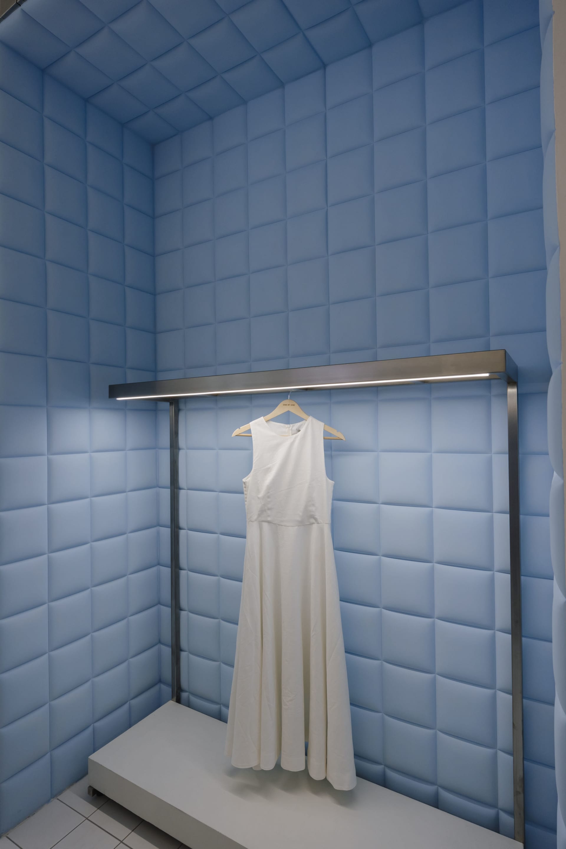 A white sleeveless dress hanging on a hanger in a blue padded wall display