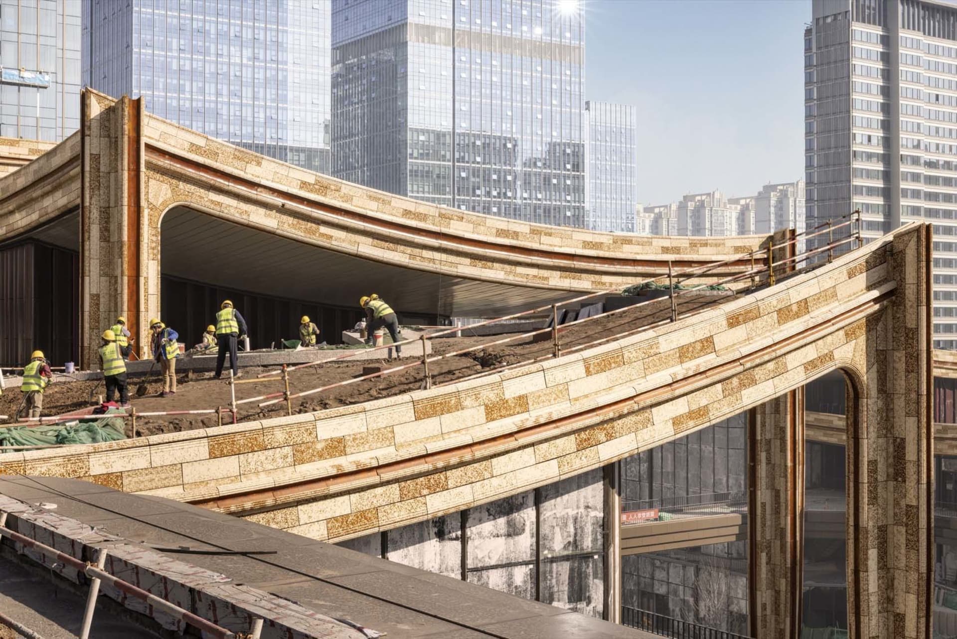 Workers at a construction site wearing safety vests and helmets on a curved tiled roof structure.