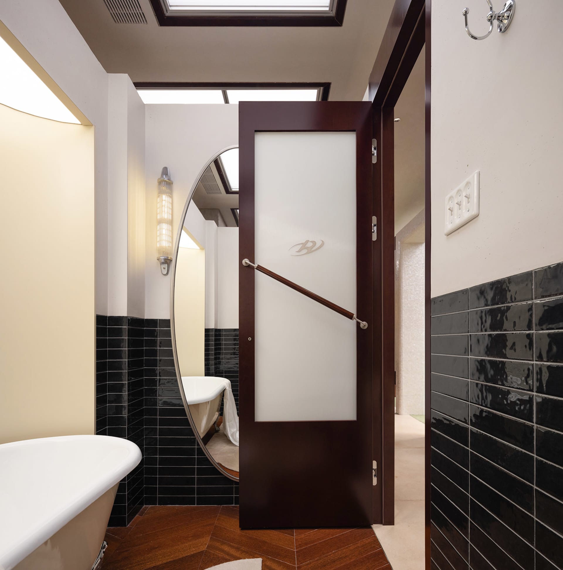 Modern bathroom with black tiles and white ceramic fixtures, featuring a dark wooden door with a grab bar.