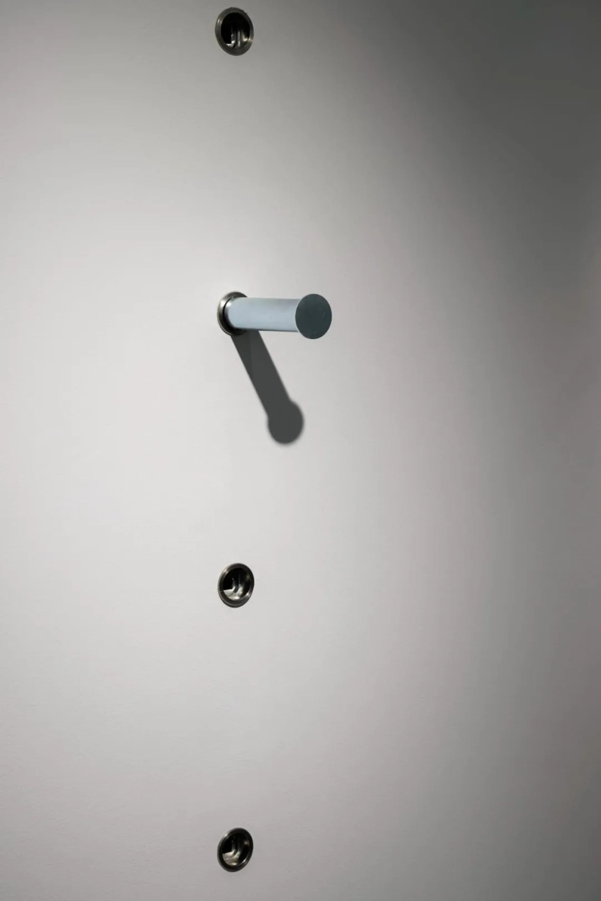 A metal lock with a gray cylinder handle attached to a smooth, white surface.