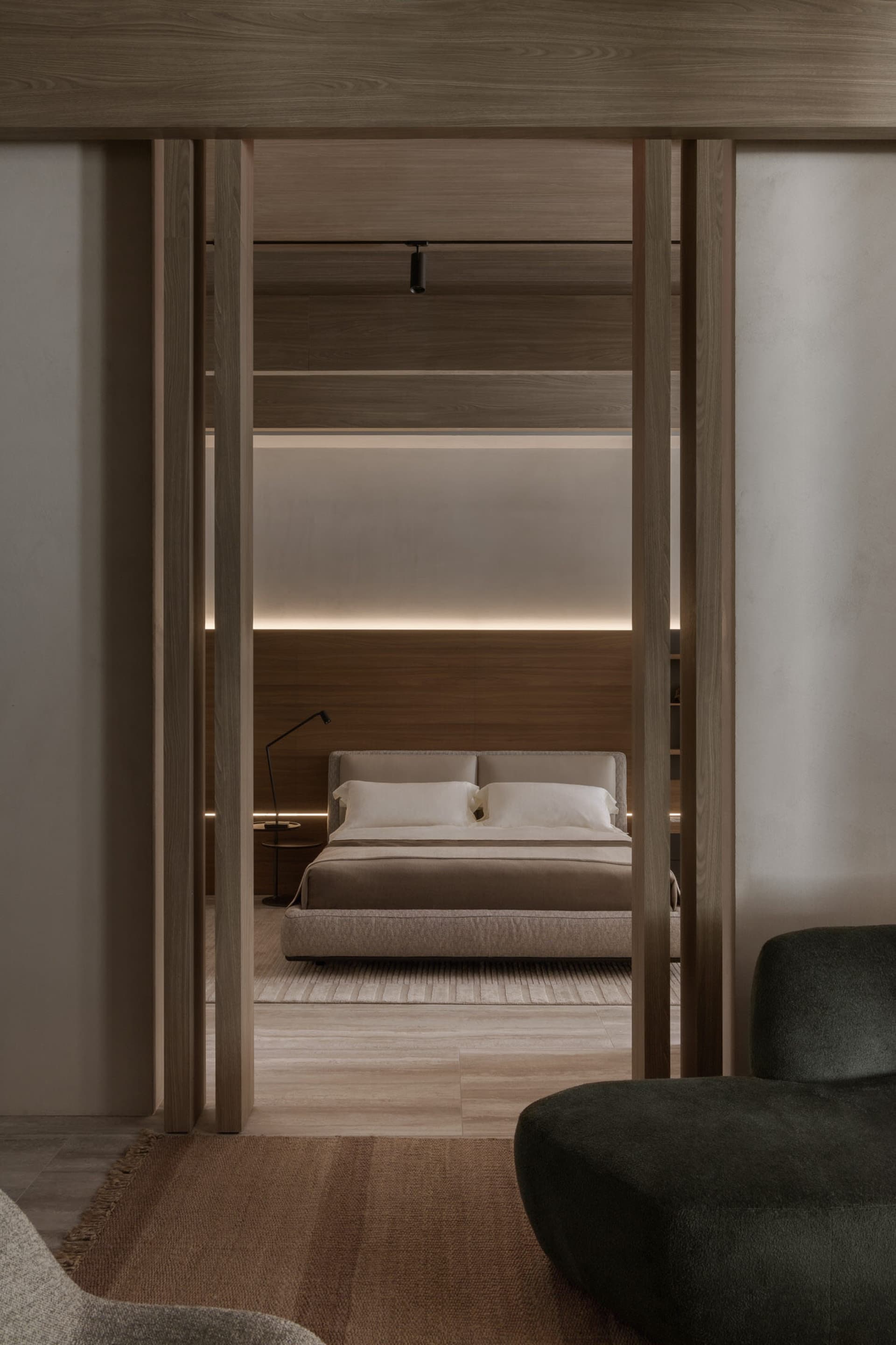 A modern minimalist bedroom featuring a low-profile bed, white linens, and a soft green ottoman.