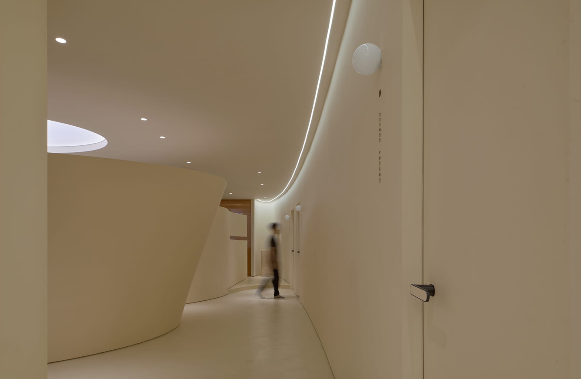 A modern office hallway with minimalistic design, white concrete walls, and a single person walking.