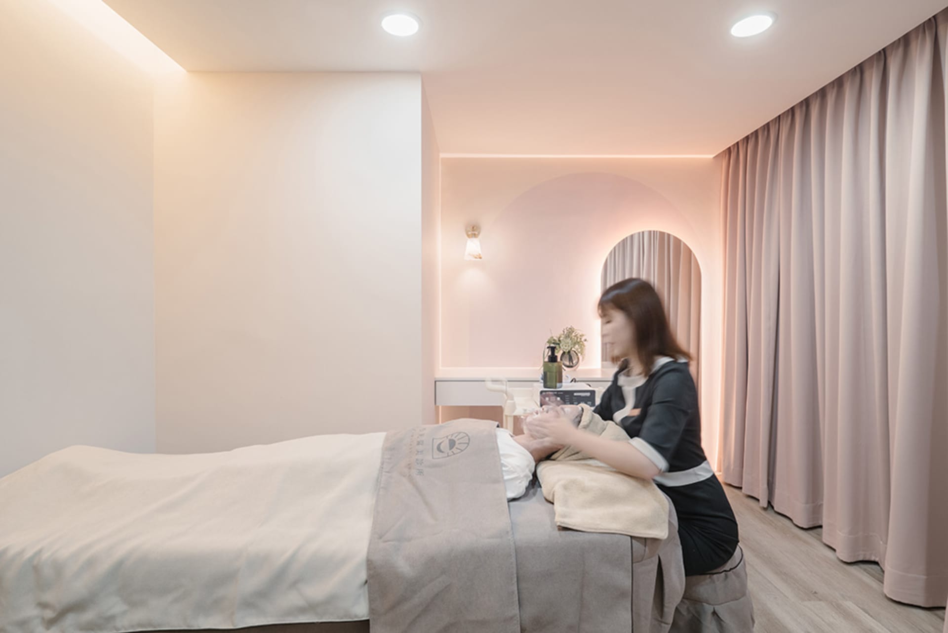 A serene spa room with neutral tones and soft lighting, featuring a massage bed and aesthetically pleasing decor.