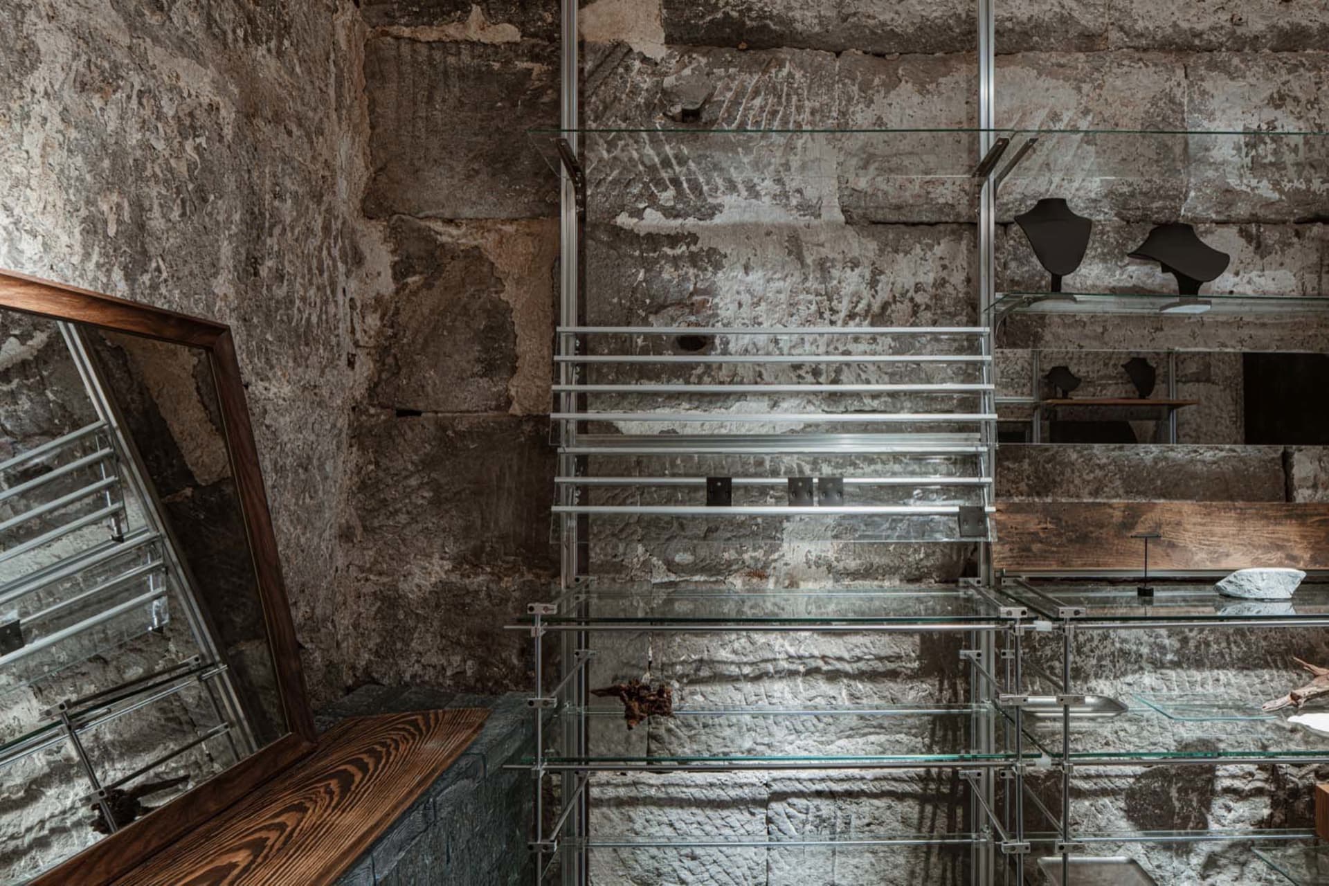 An industrial-style glass display case against a textured stone wall, featuring glass shelves and metal supports.