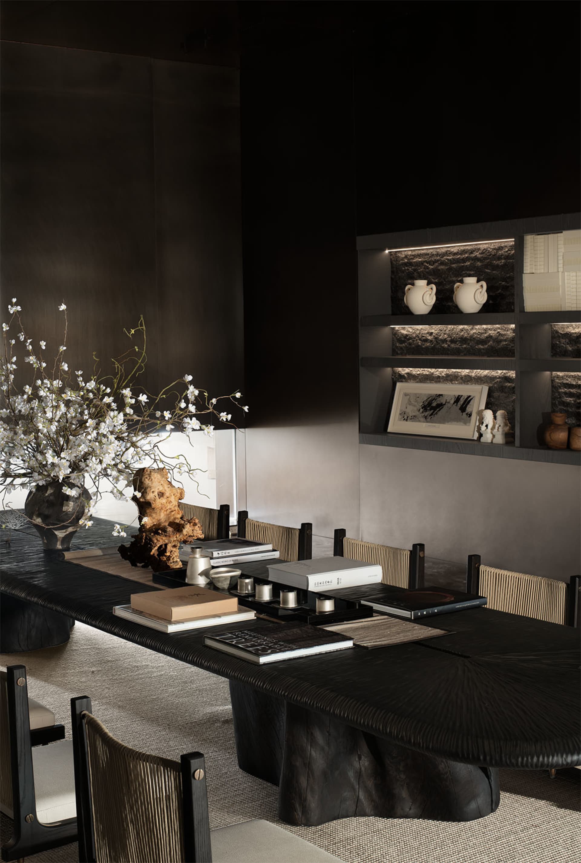 A modern dining room featuring black furniture and a vase with white flowers.