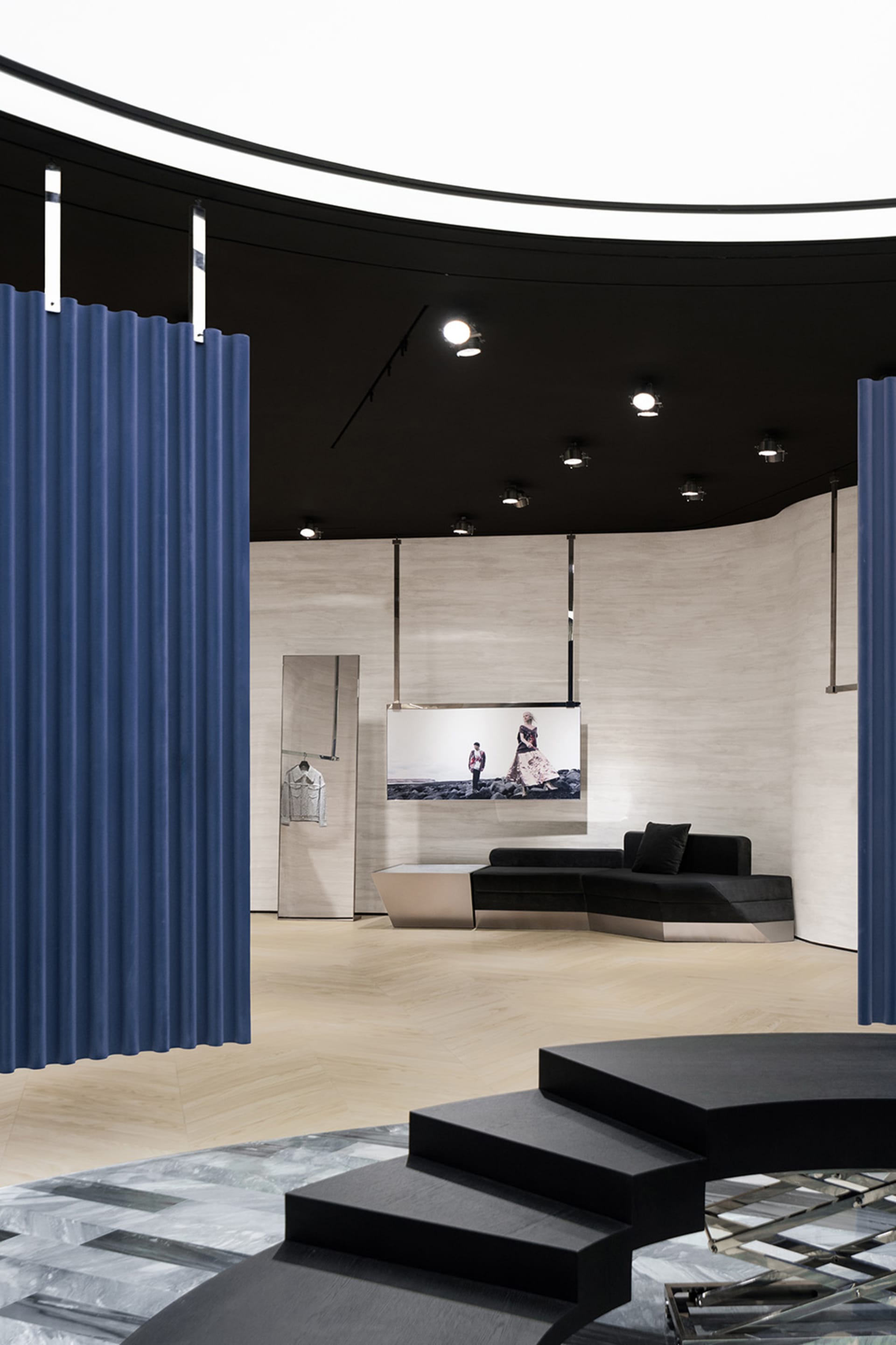 Modern pop-up store with concrete and glass materials, featuring a black sofa and blue curtains.