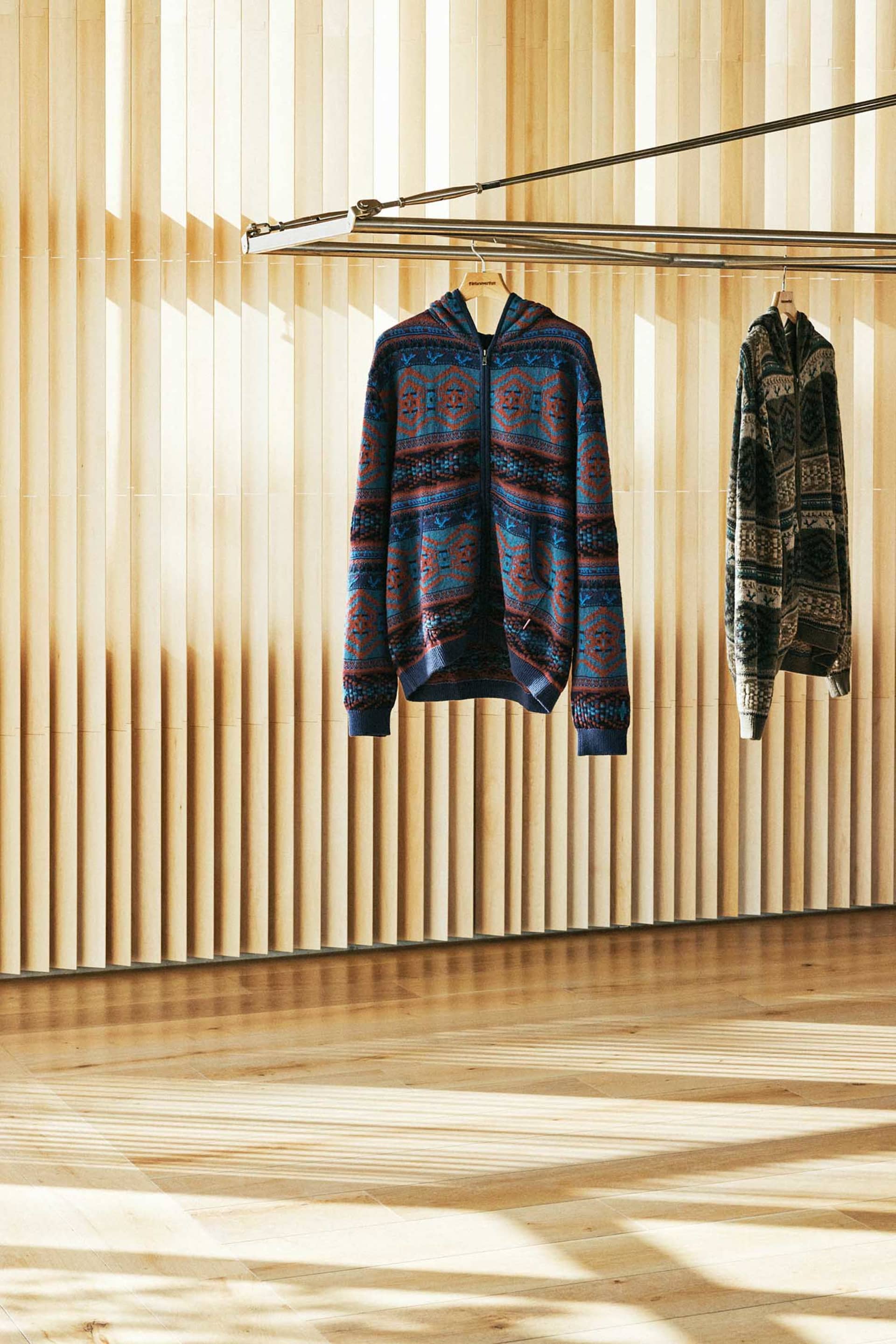 一件藍棕幾何圖案毛衣懸掛在木質牆面上的服裝展示。