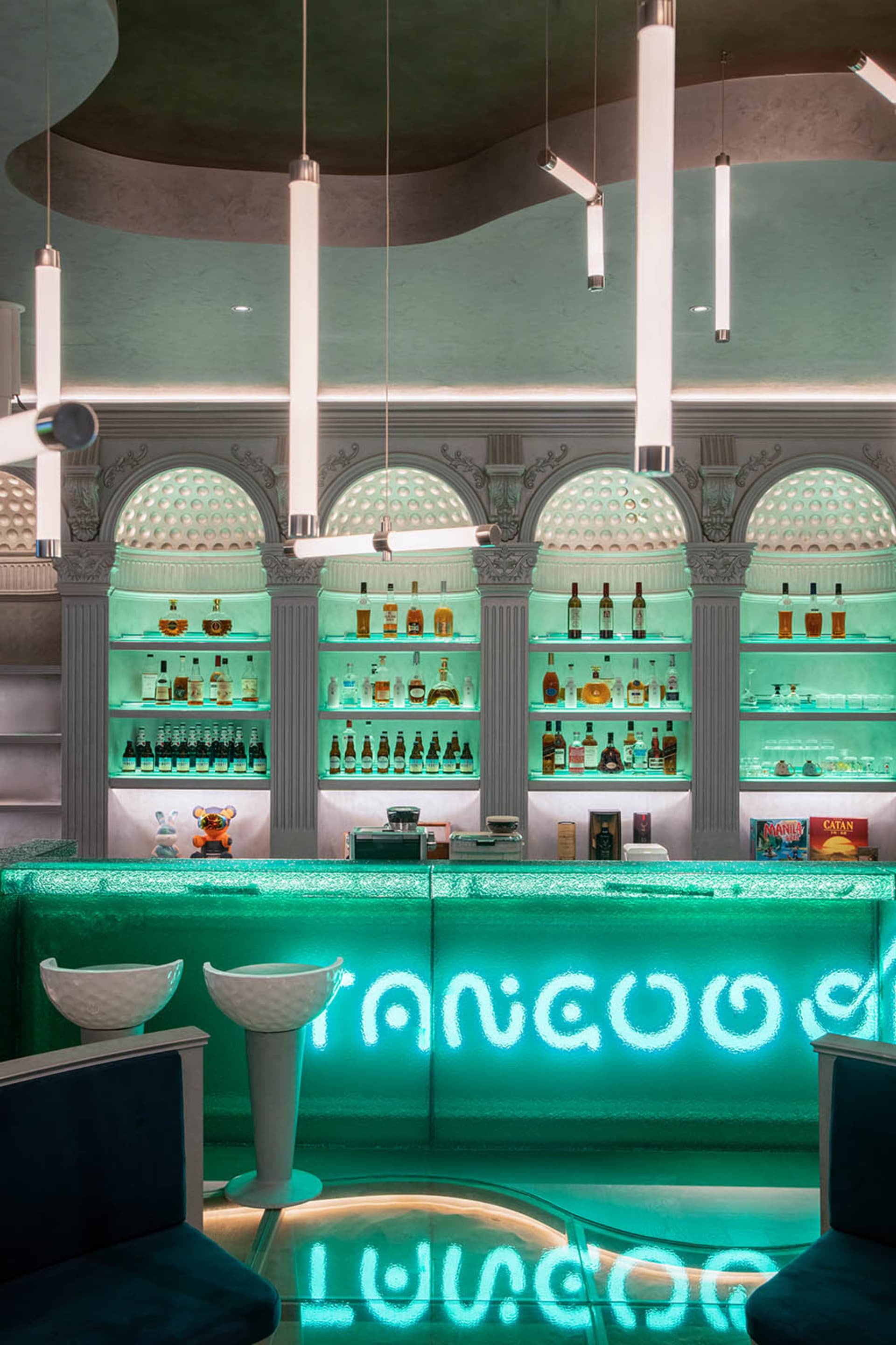 A brightly lit modern bar with green furniture and shelves filled with bottles.