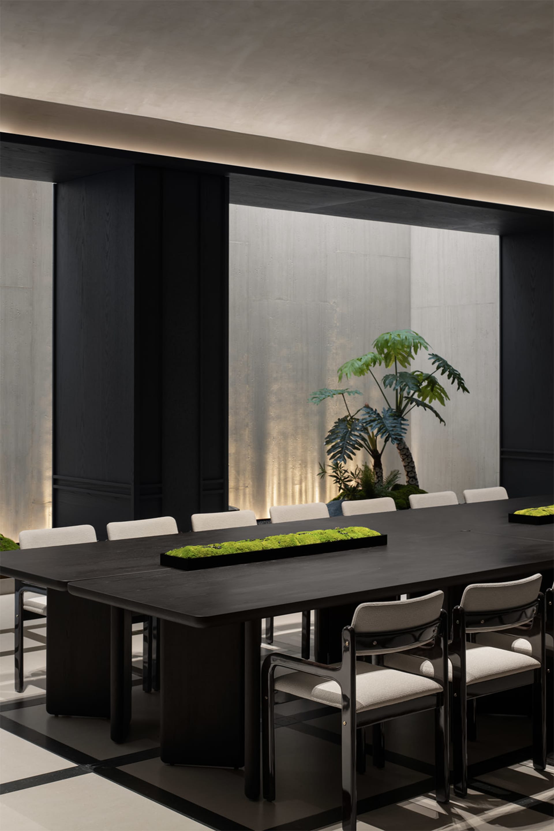 A modern conference room featuring a long black table surrounded by white chairs, with a central green plant arrangement and