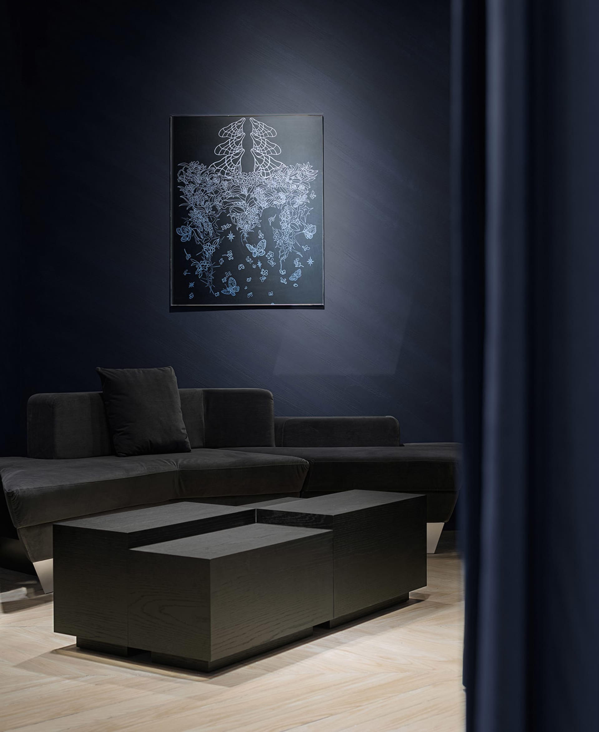 Modern living room featuring a dark grey sofa, a wooden coffee table, and a framed artwork on the dark blue wall.