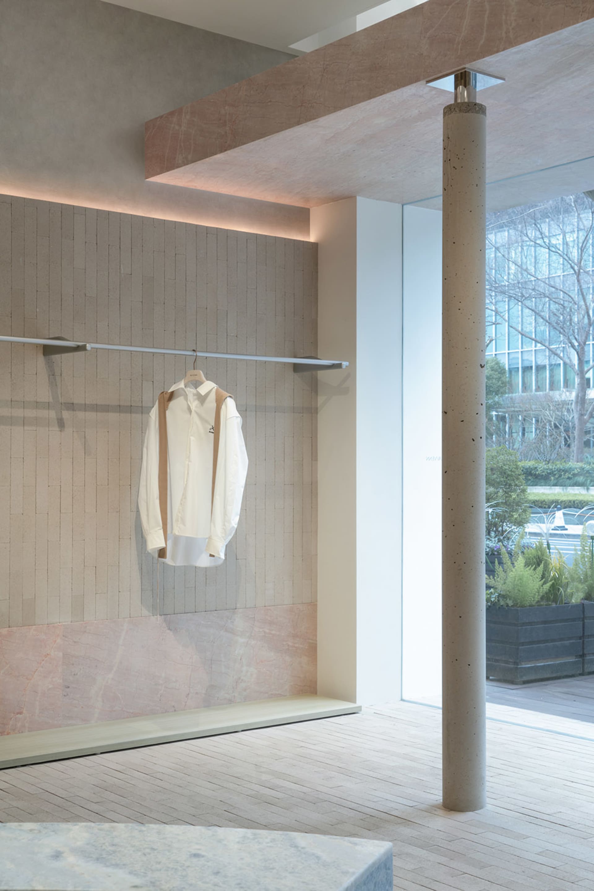現代服飾店展示，採用淺色混凝土牆面，單件白色襯衫懸掛於橫桿上。