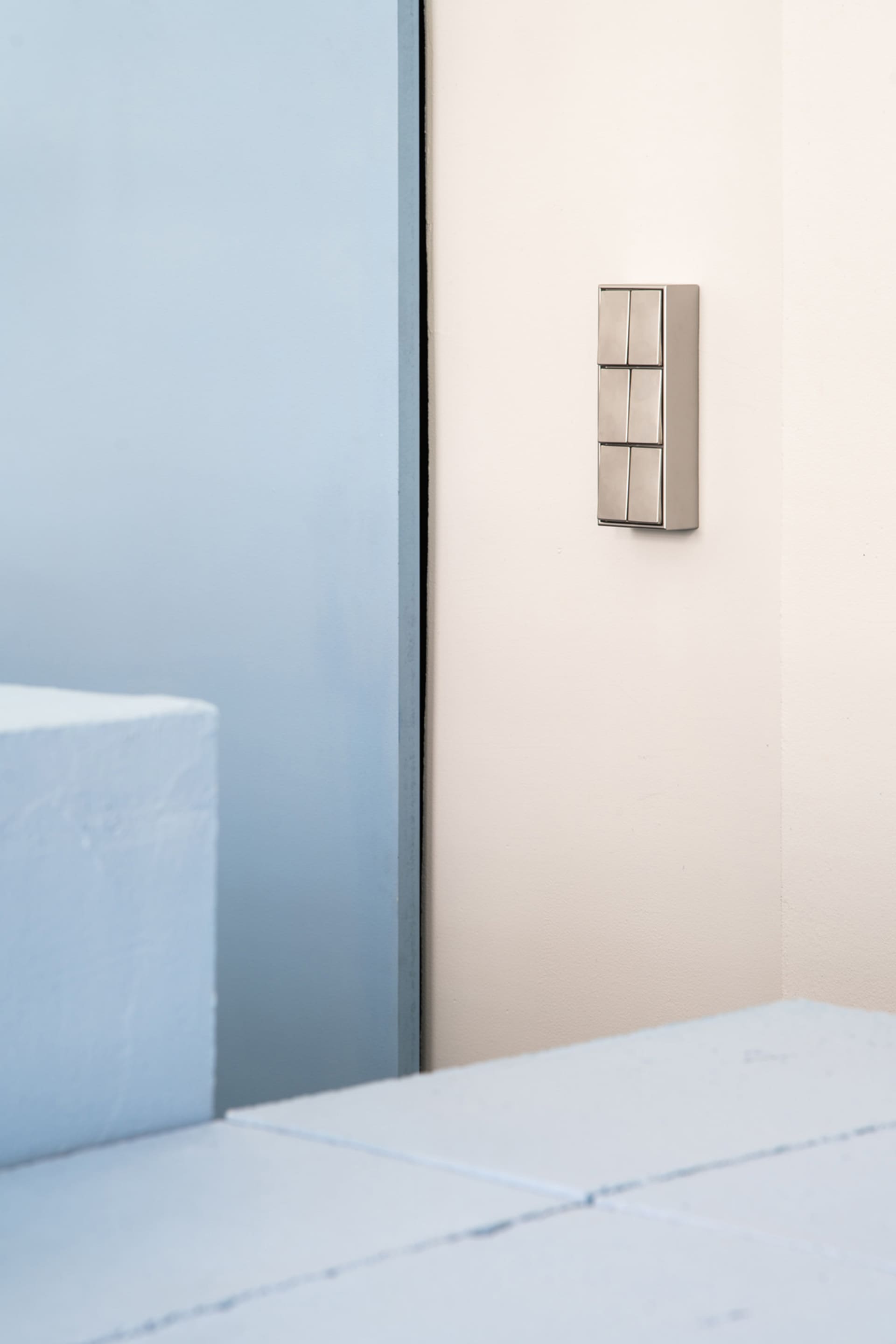A minimalist doorbell mounted on a white wall, featuring metallic material.