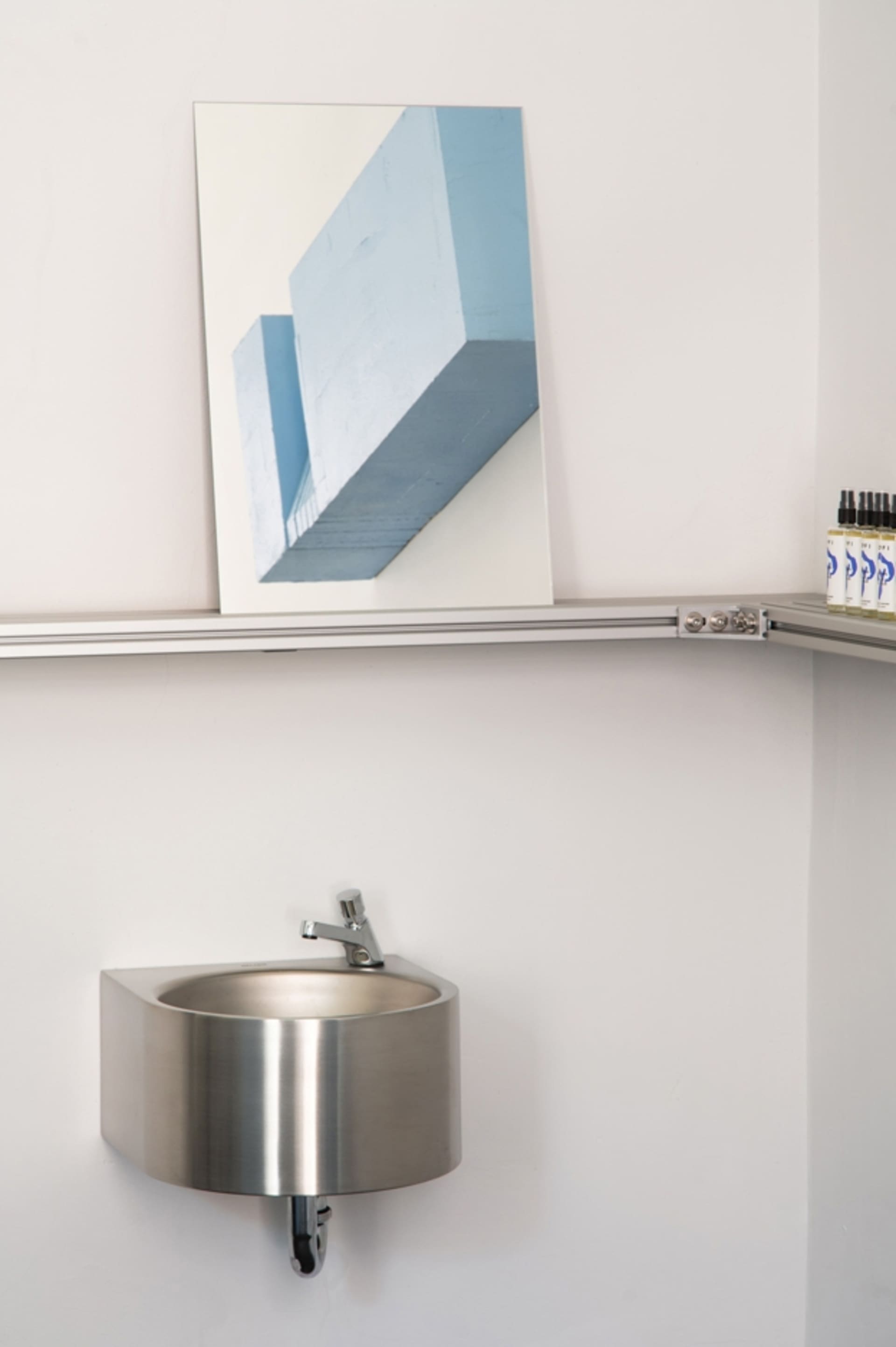 A modern industrial bathroom featuring a metal sink and shelf with a framed blue artwork on the wall.