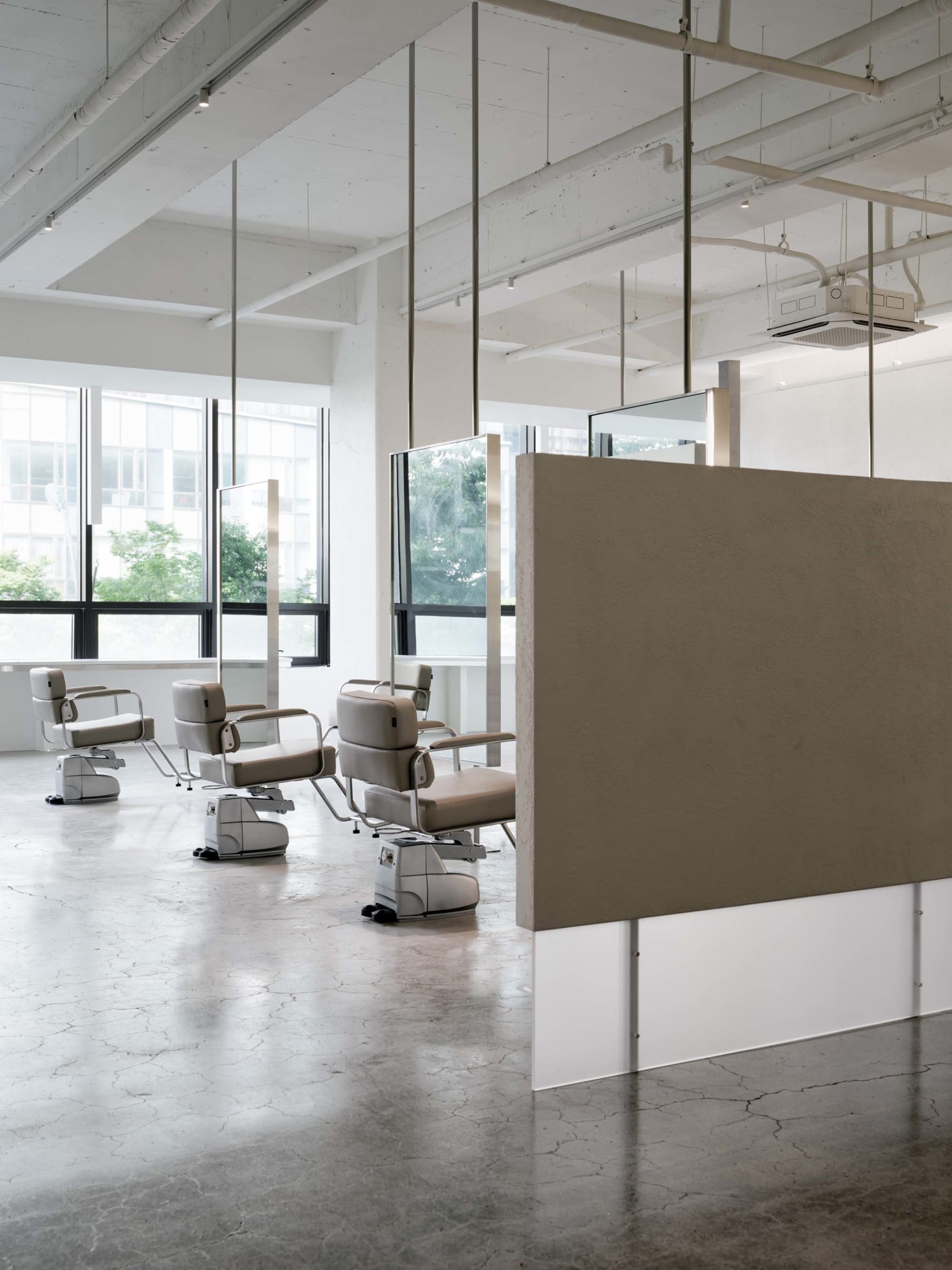 An industrial-style salon with concrete floor, metal chairs, and glass partitions.