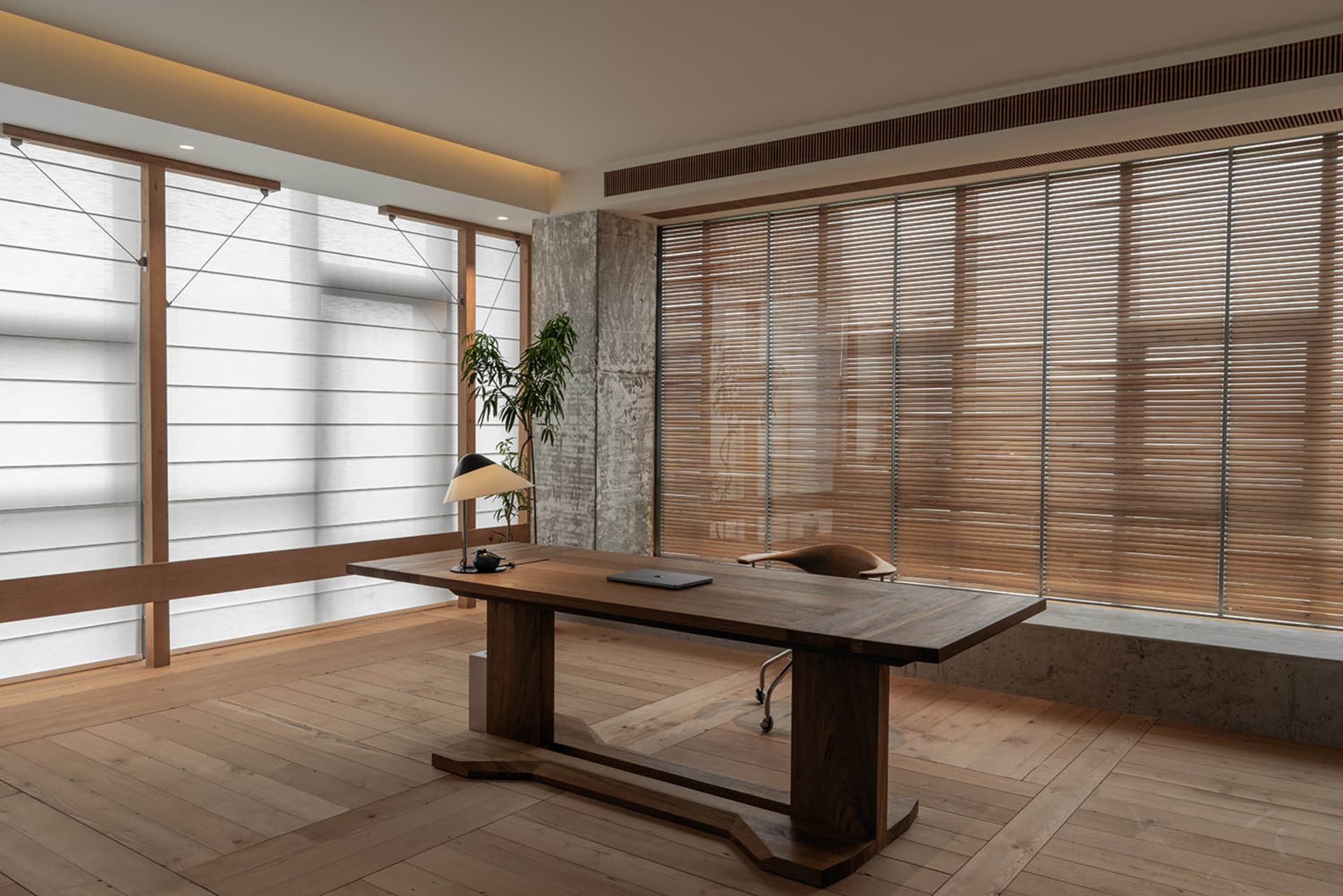 Modern minimalist office space featuring a wooden desk, desk lamp, and wooden floor, with concrete walls and light wooden bli