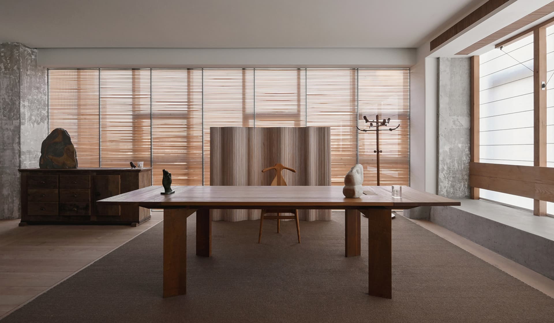 A modern home office with a wooden table, concrete walls, and natural wood finishes.