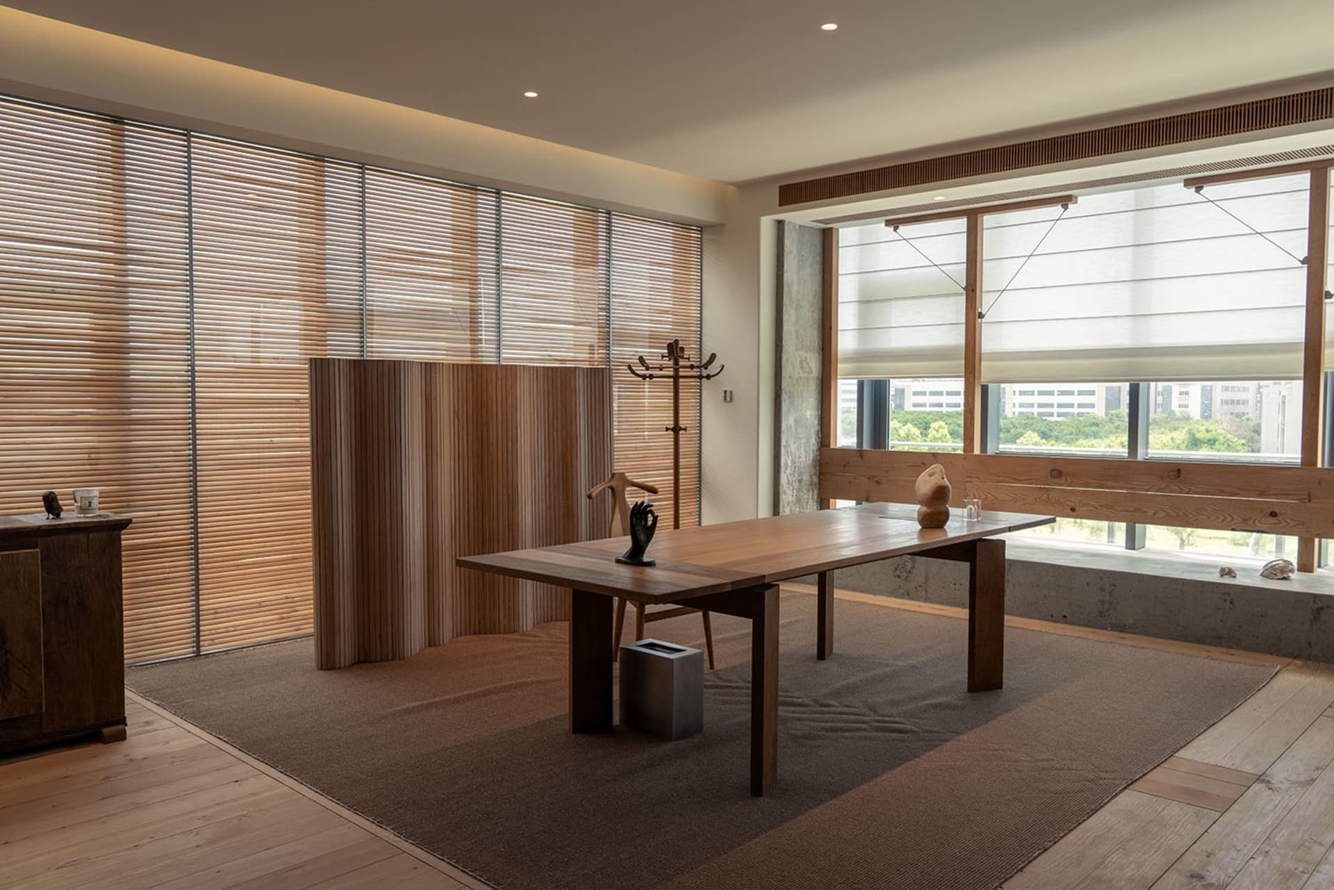 A minimalist living room featuring wooden furniture, large windows, and a serene atmosphere.