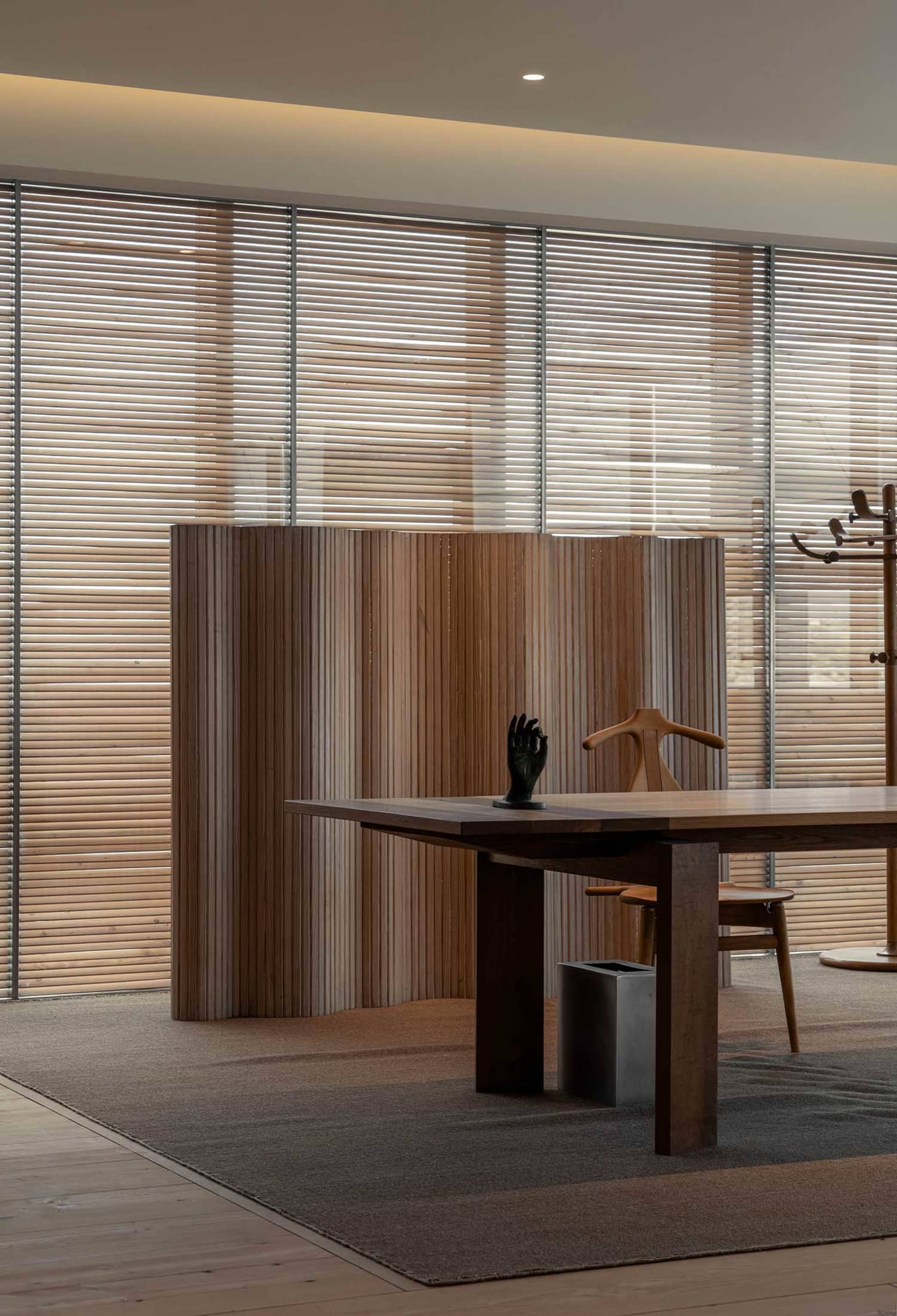 A modern dining room featuring a wooden table with a minimalist design and a wooden chair in front of a large window with woo