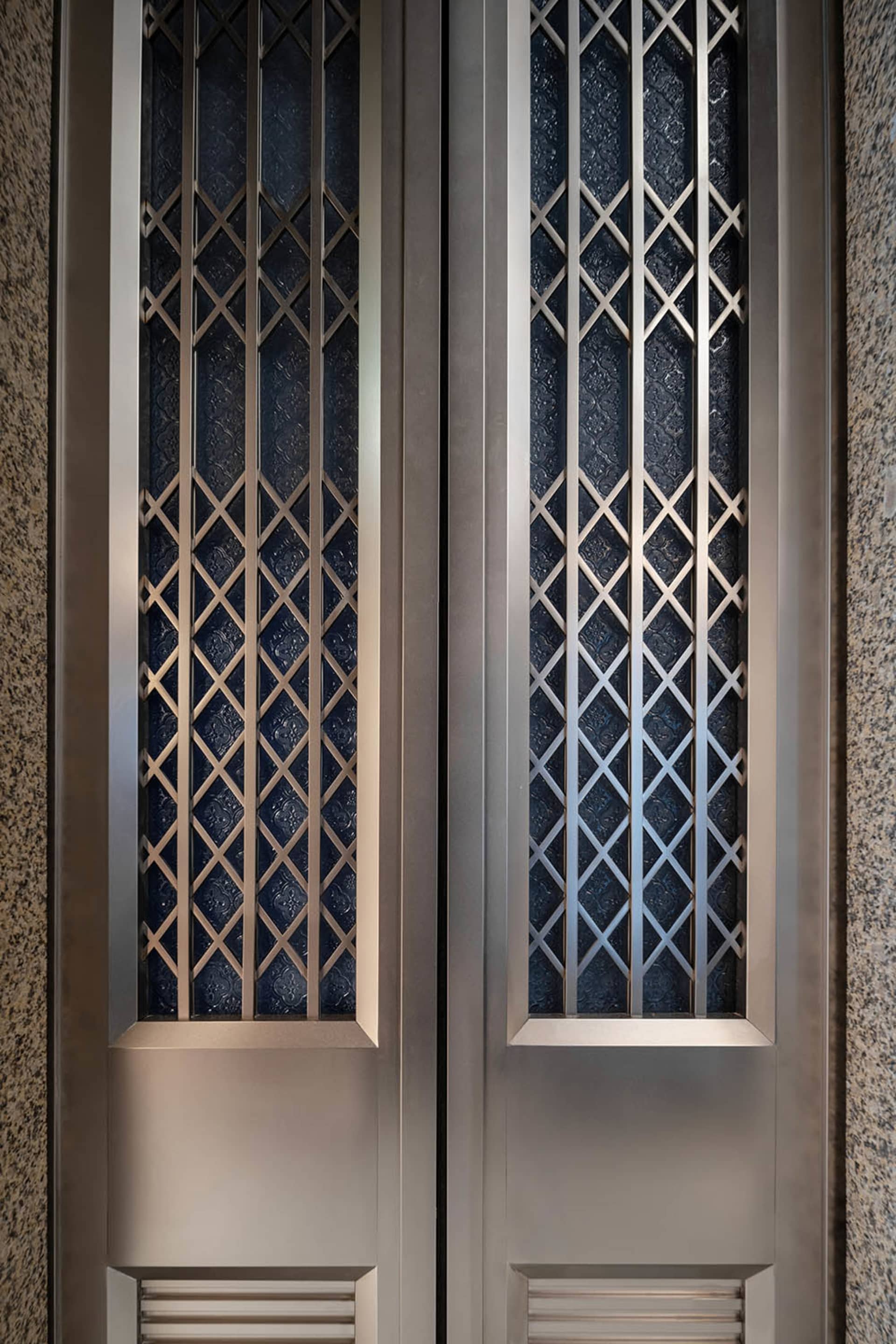 A modern metallic door featuring intricate lattice patterns and textured glass panels.