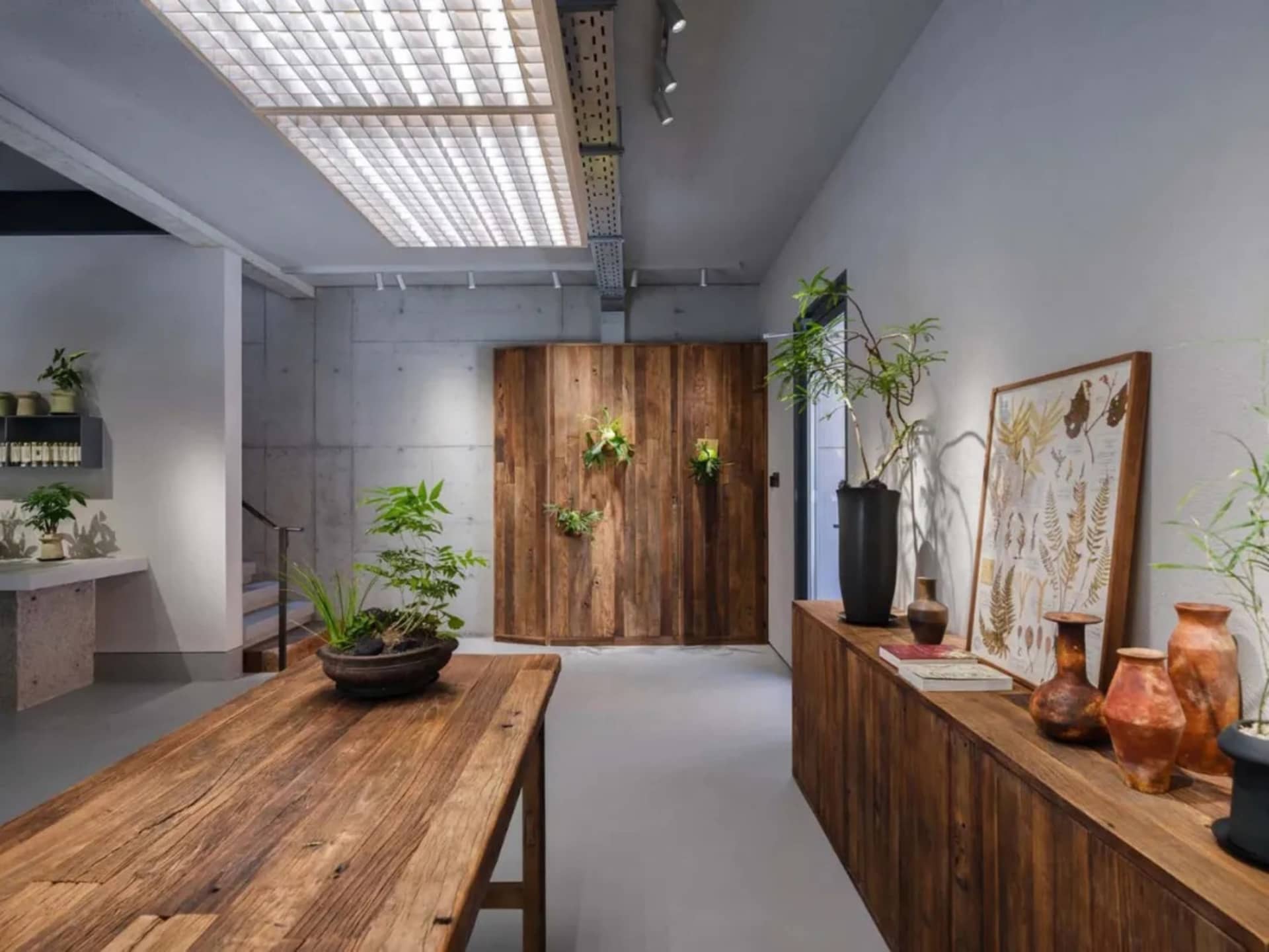 An industrial retail space featuring wooden tables and a concrete wall with plants and vases.