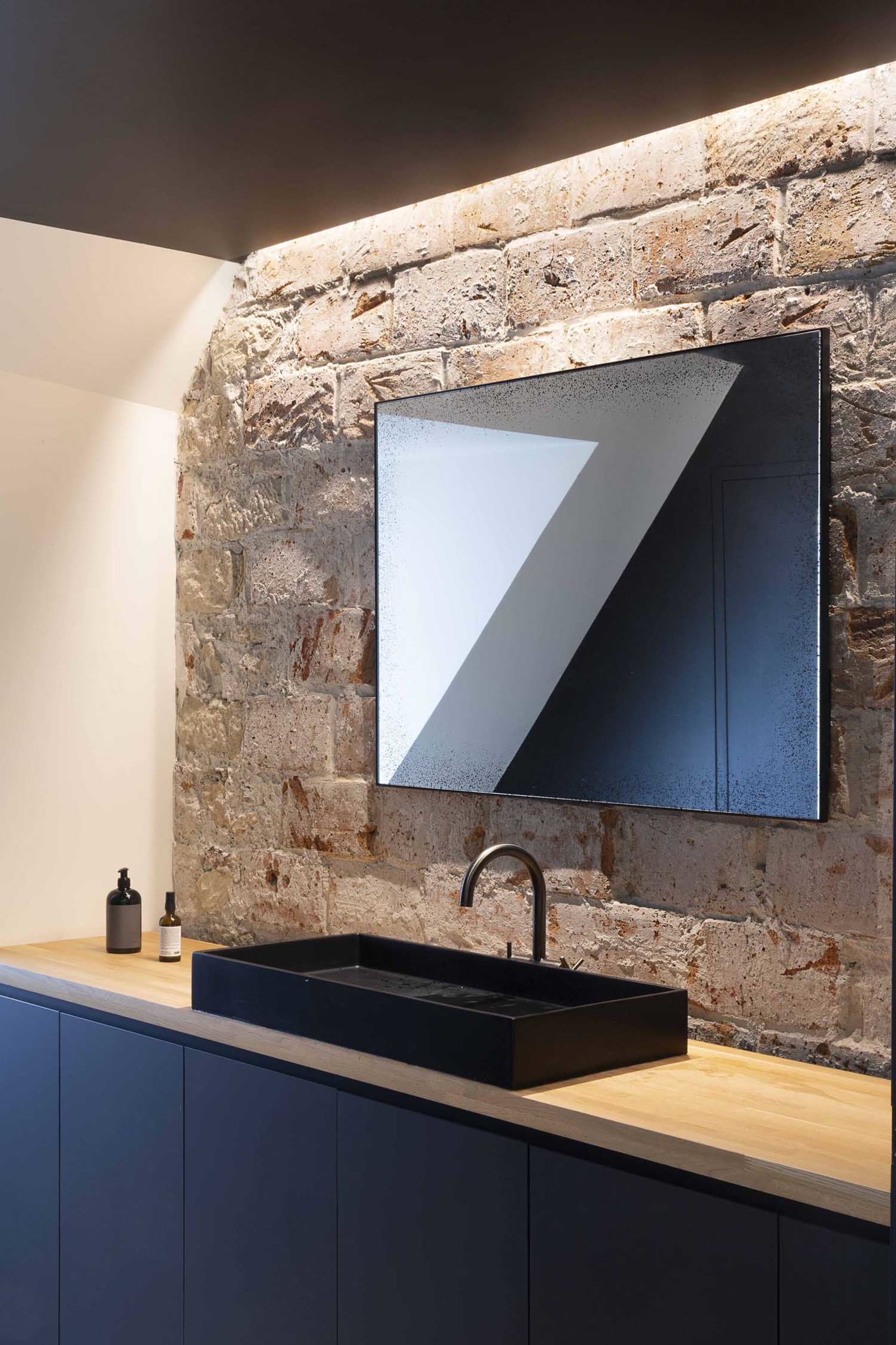 A modern bathroom featuring a black sink and faucet on a wooden counter against a brick wall with a skylight.