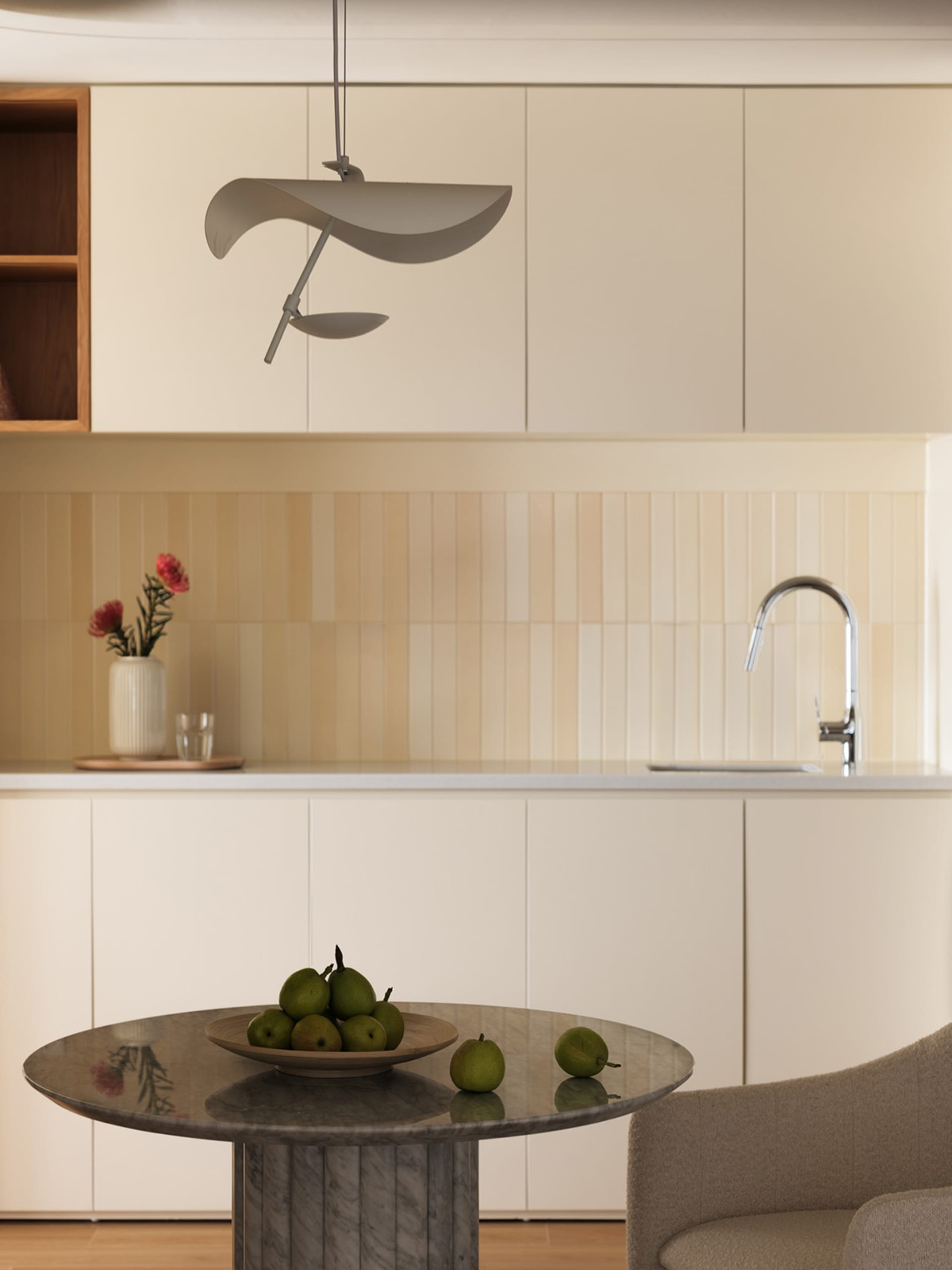 A modern minimalist kitchen with a round marble table topped with a wooden bowl filled with green pears, against a backdrop o