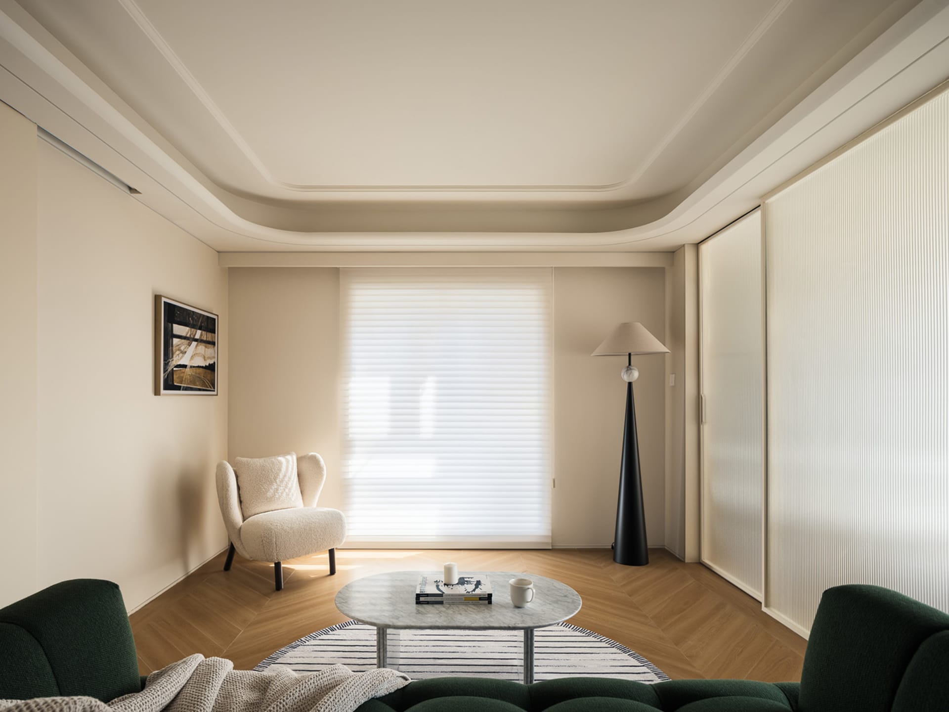 Minimalist living room with wooden furniture and flooring, featuring a white armchair, a green sofa, and a round marble coffe