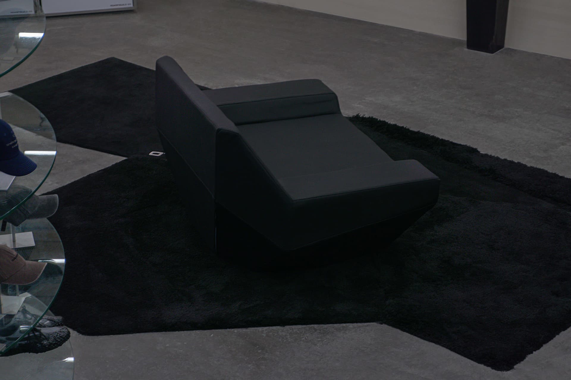 A black leather lounge chair placed on a black rug in a minimalist room setting.