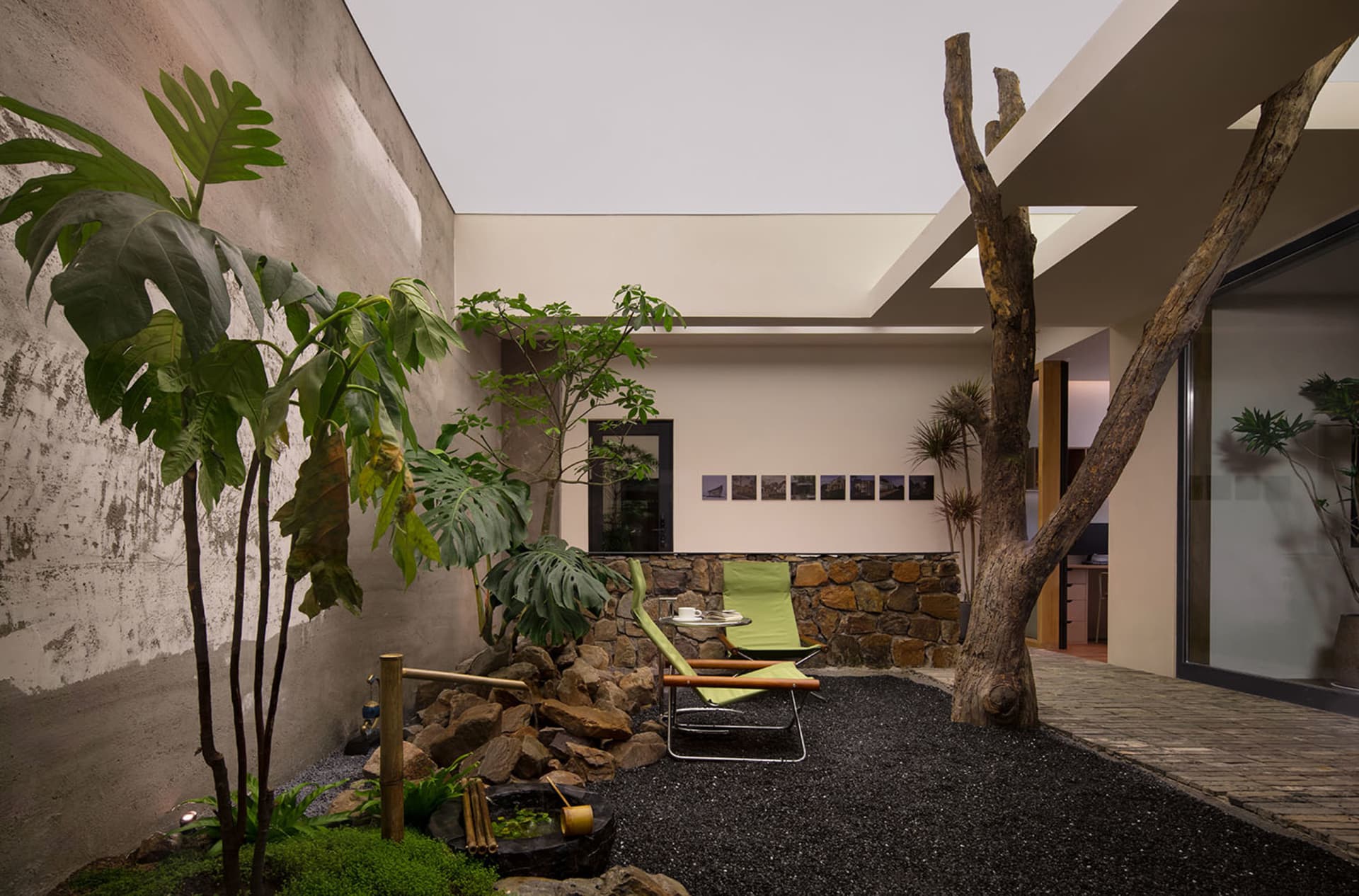 Modern living room with concrete walls, rock landscaping, and green outdoor furniture.