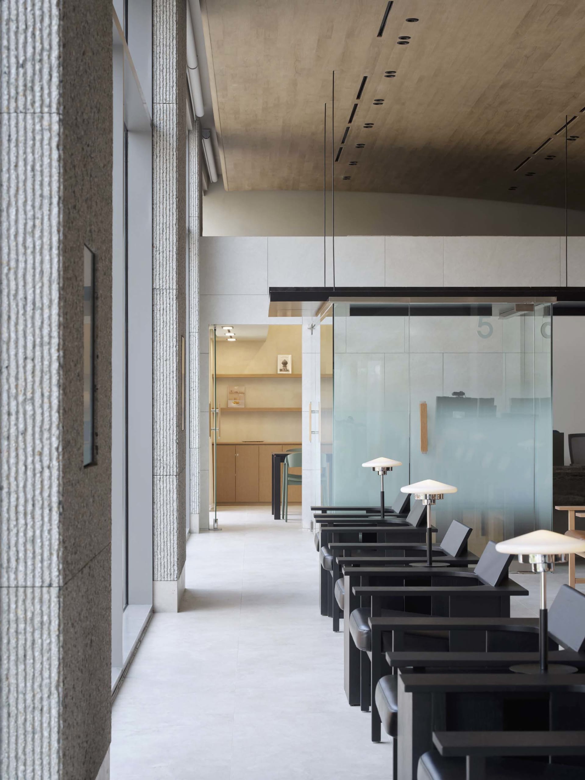 A modern cafe interior featuring a black metal frame storefront, concrete floor, and a terrazzo counter.