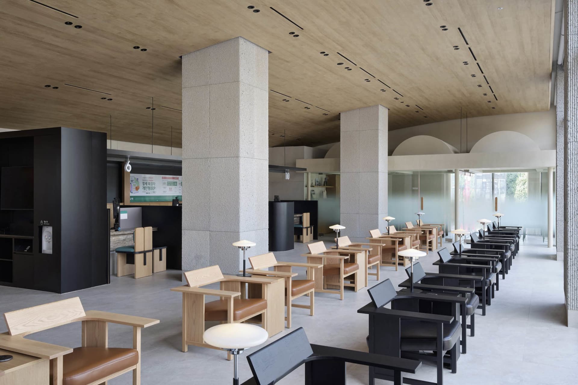 Interior of a modern coffee shop featuring wooden furniture, concrete columns, and large glass windows.