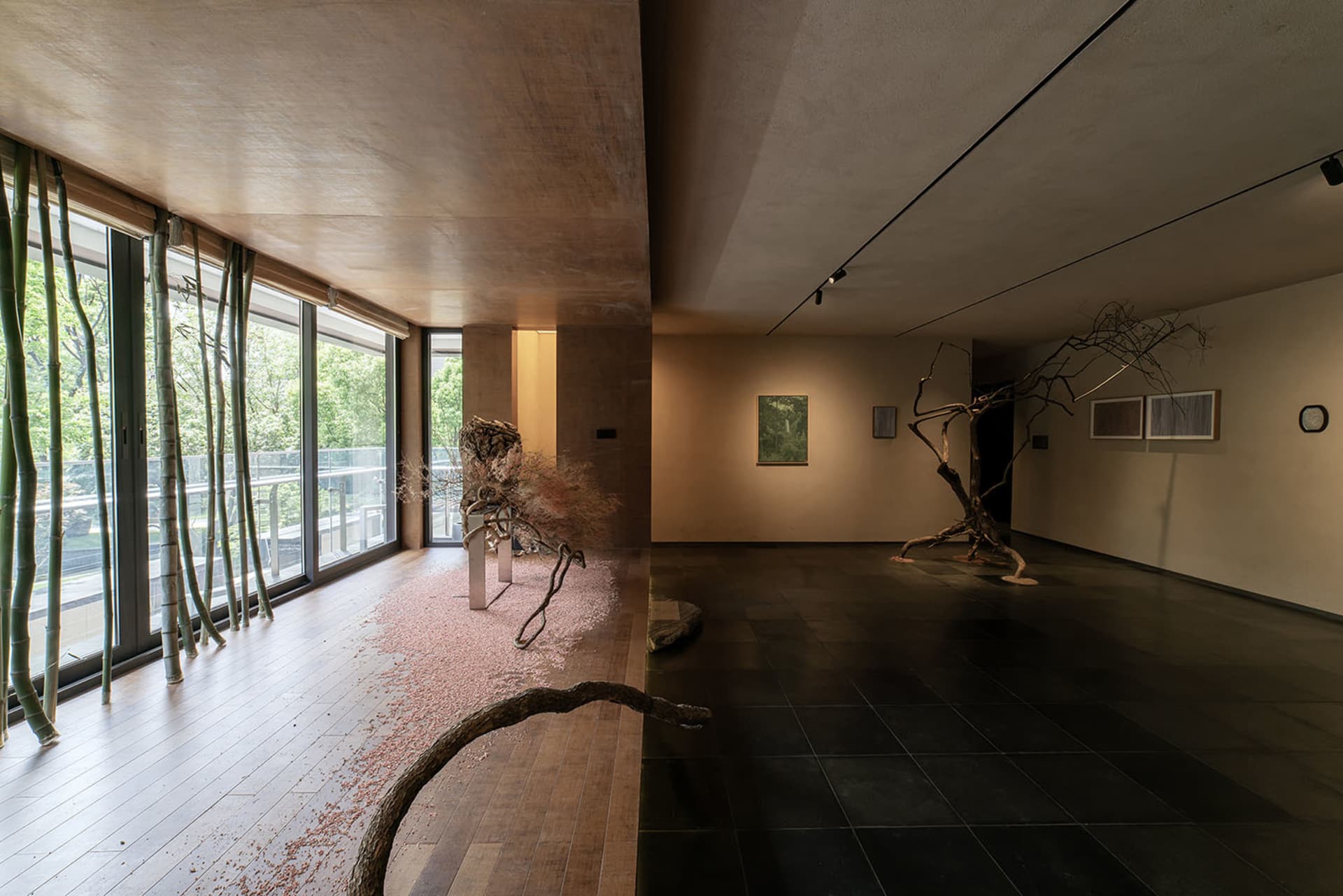 A spacious art gallery with minimalist decor featuring dry tree branches as central elements and a view of the outdoors.