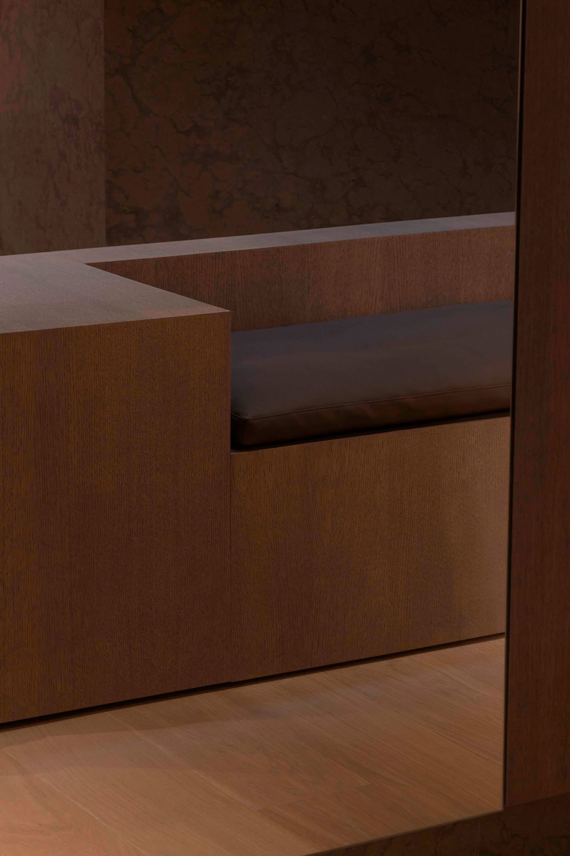 Modern interior design featuring a wooden bench with brown leather cushions and marble walls.