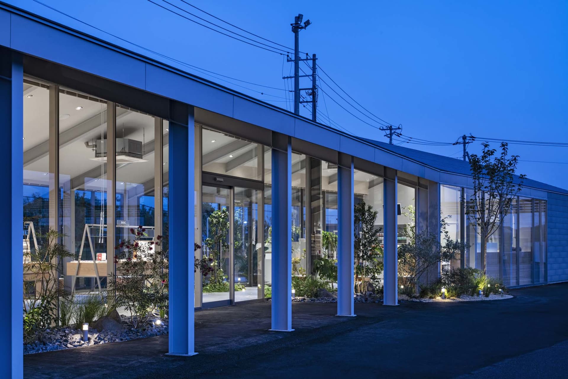 A modern building with glass walls and metal structures, viewed from the street at dusk.