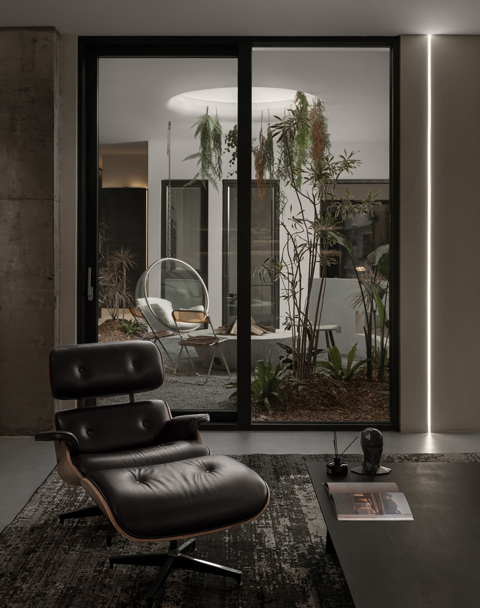 Modern living room with a black metal and leather lounge chair in front of a large window with plants.