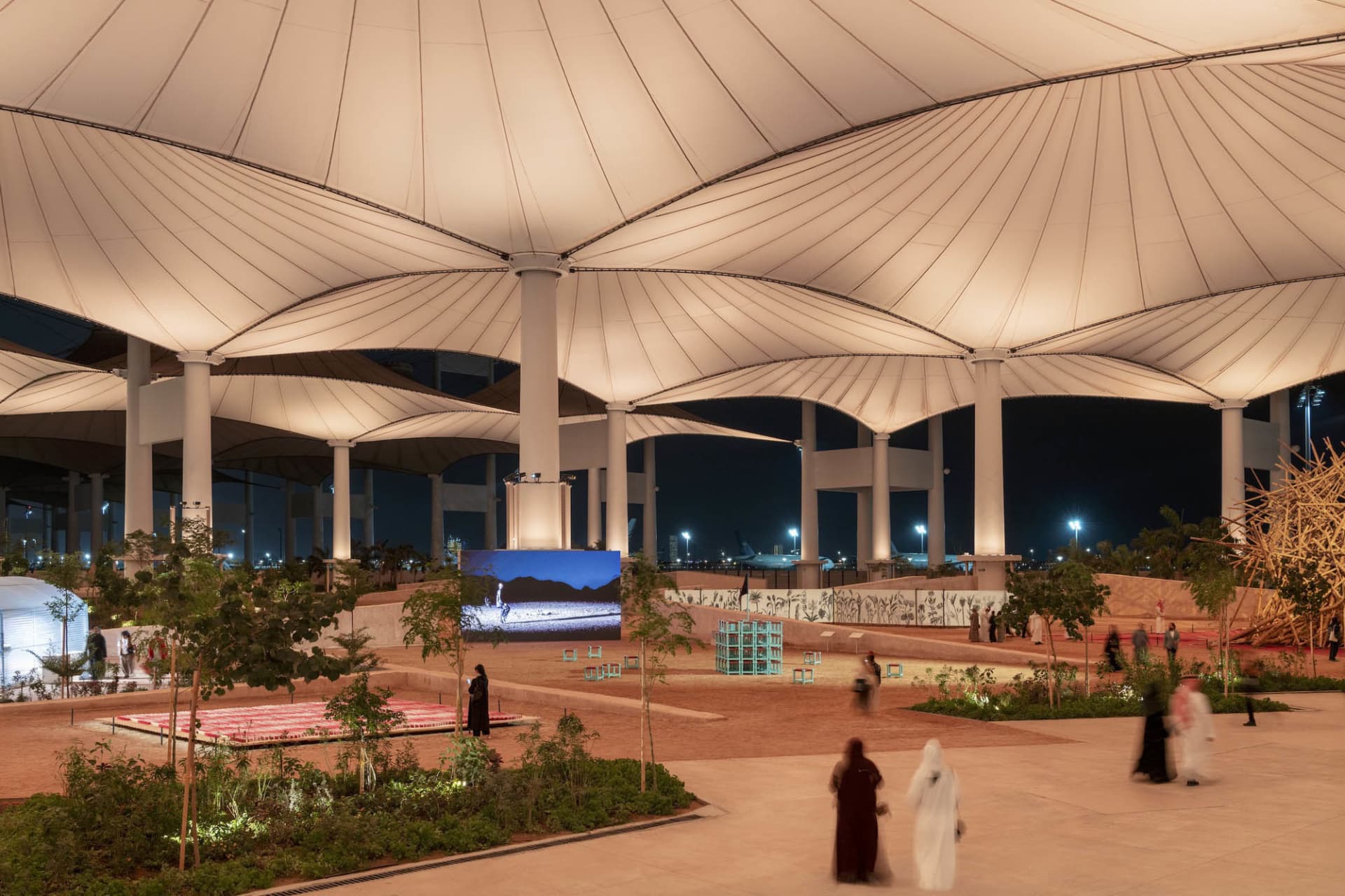 Modern, spacious urban space with a textured fabric roof structure and various functional zones.