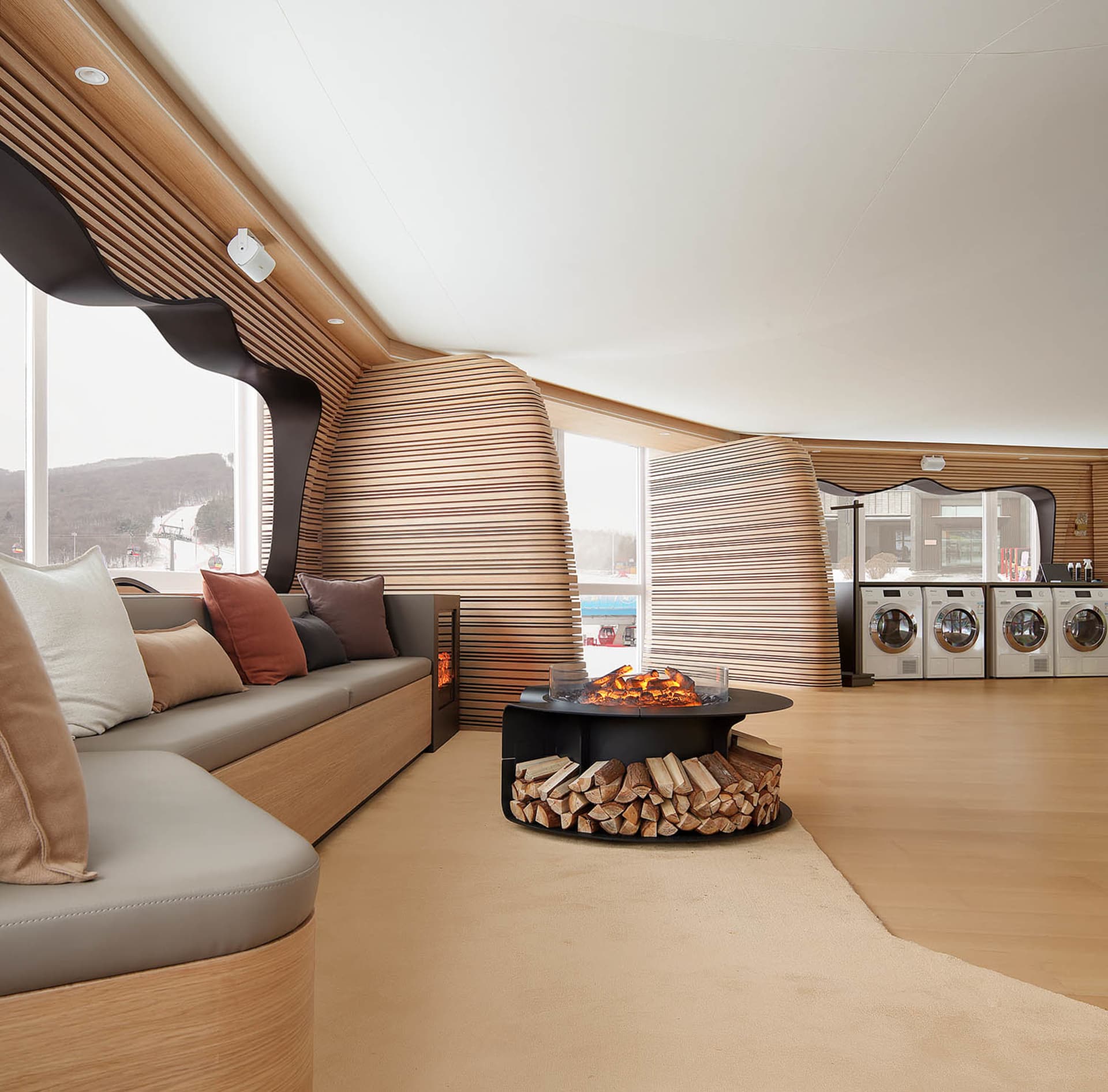 A modern living room with wooden walls, seating, and a circular fireplace with logs.
