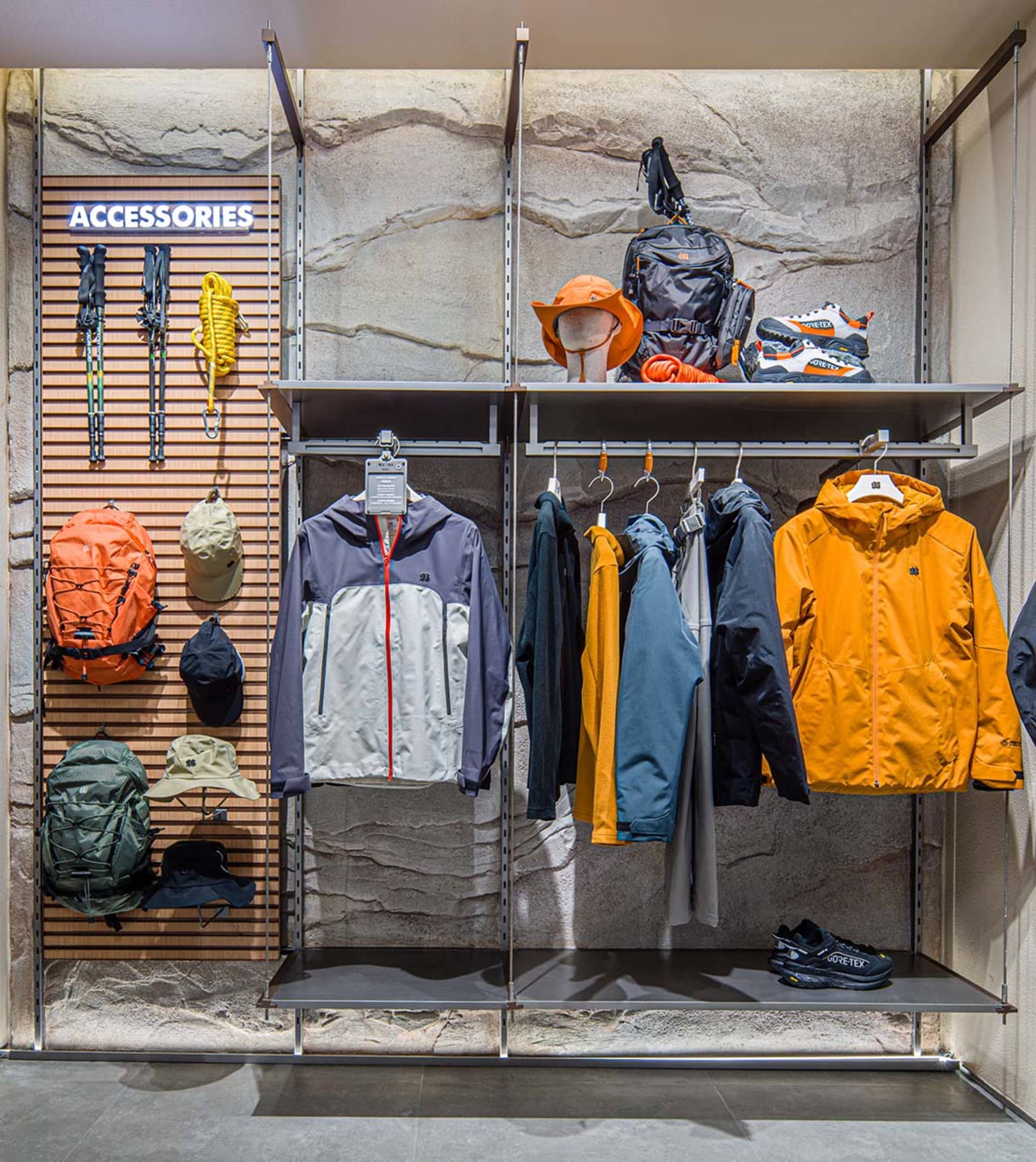 A retail store display featuring jackets and accessories arranged on metal shelves against a stone background.