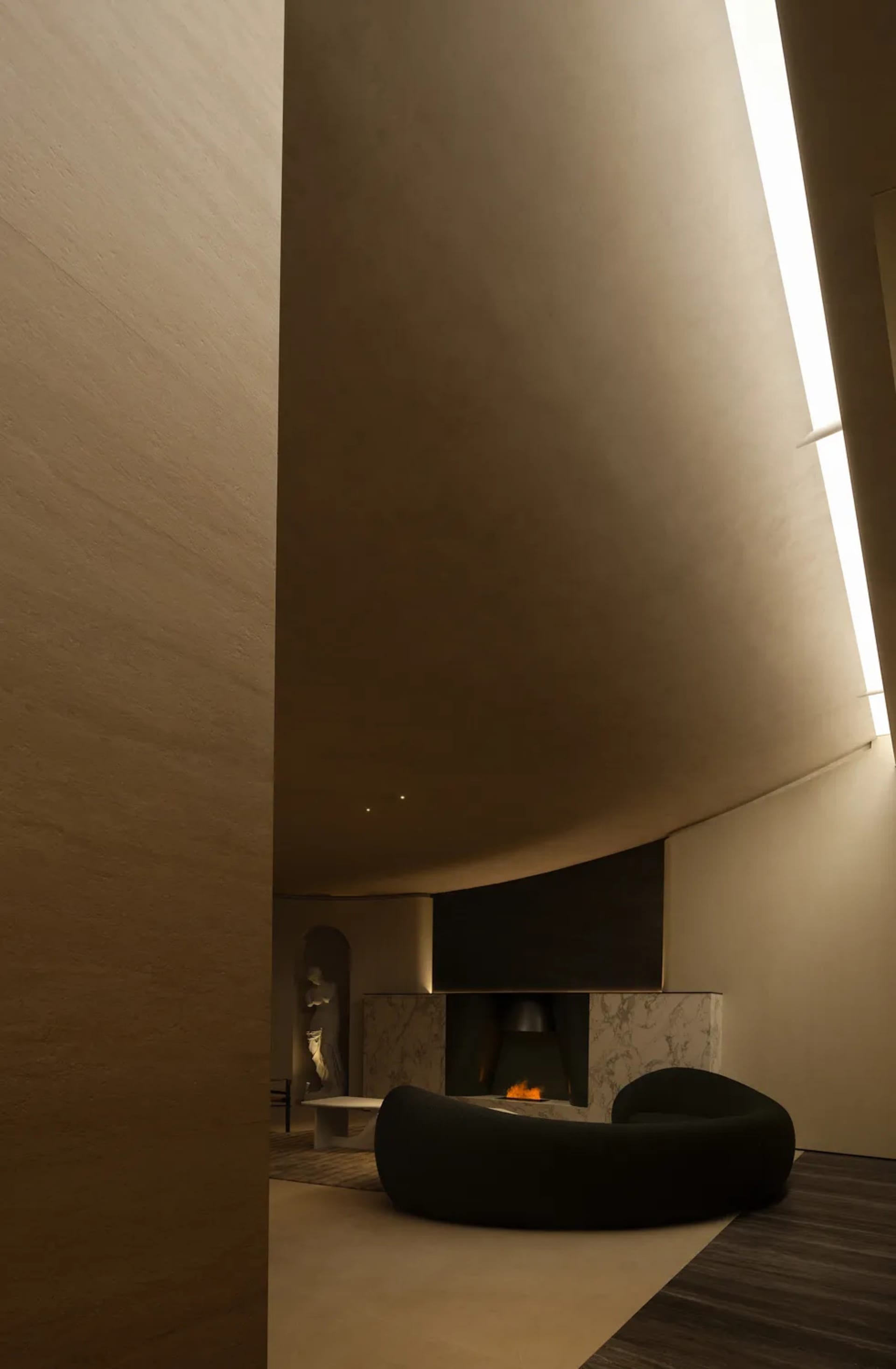 A modern living room with concrete walls, a circular sofa, and a fireplace with a small fire burning.