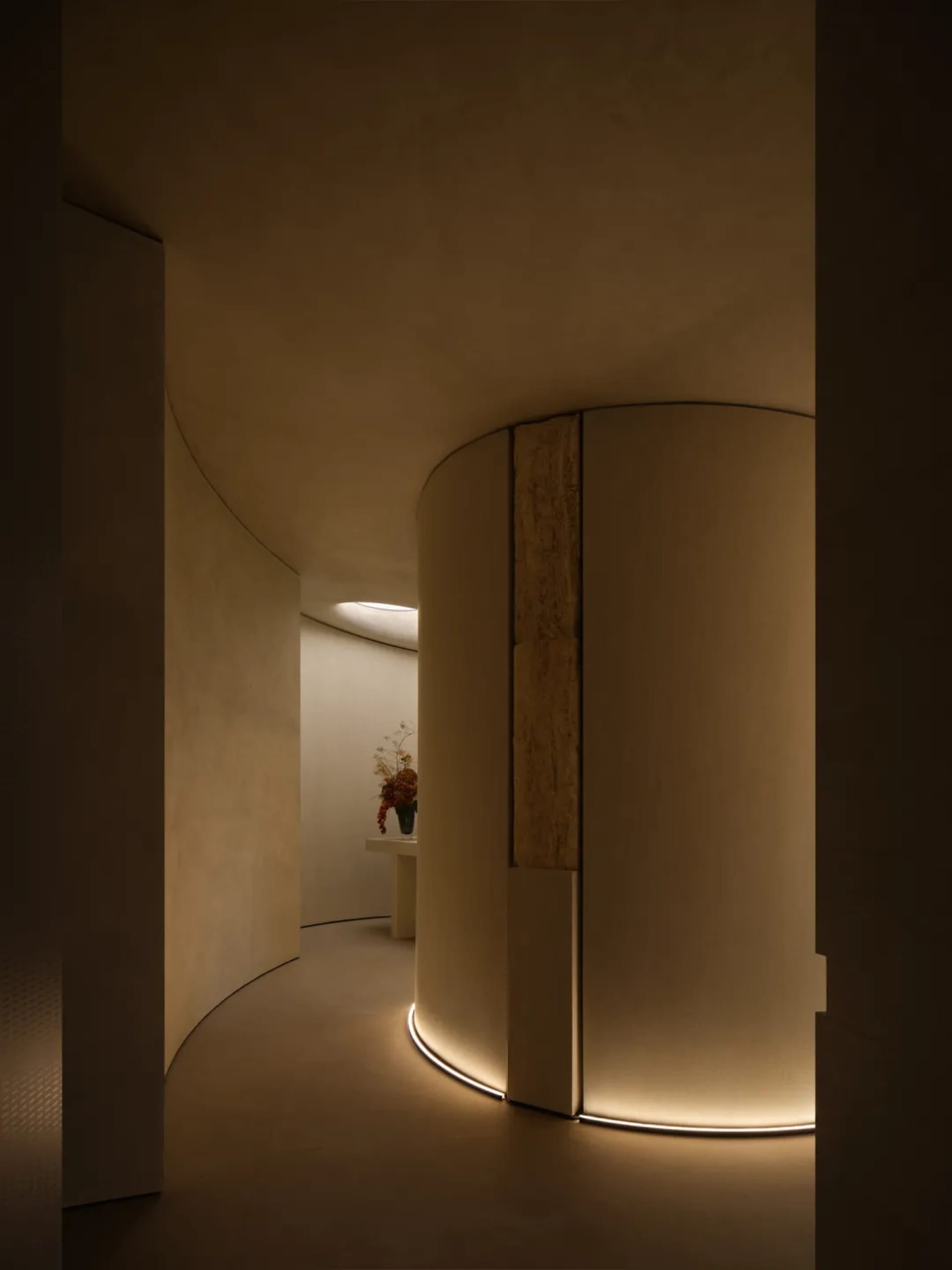 A modern corridor with curved concrete walls and illuminated floor edges.