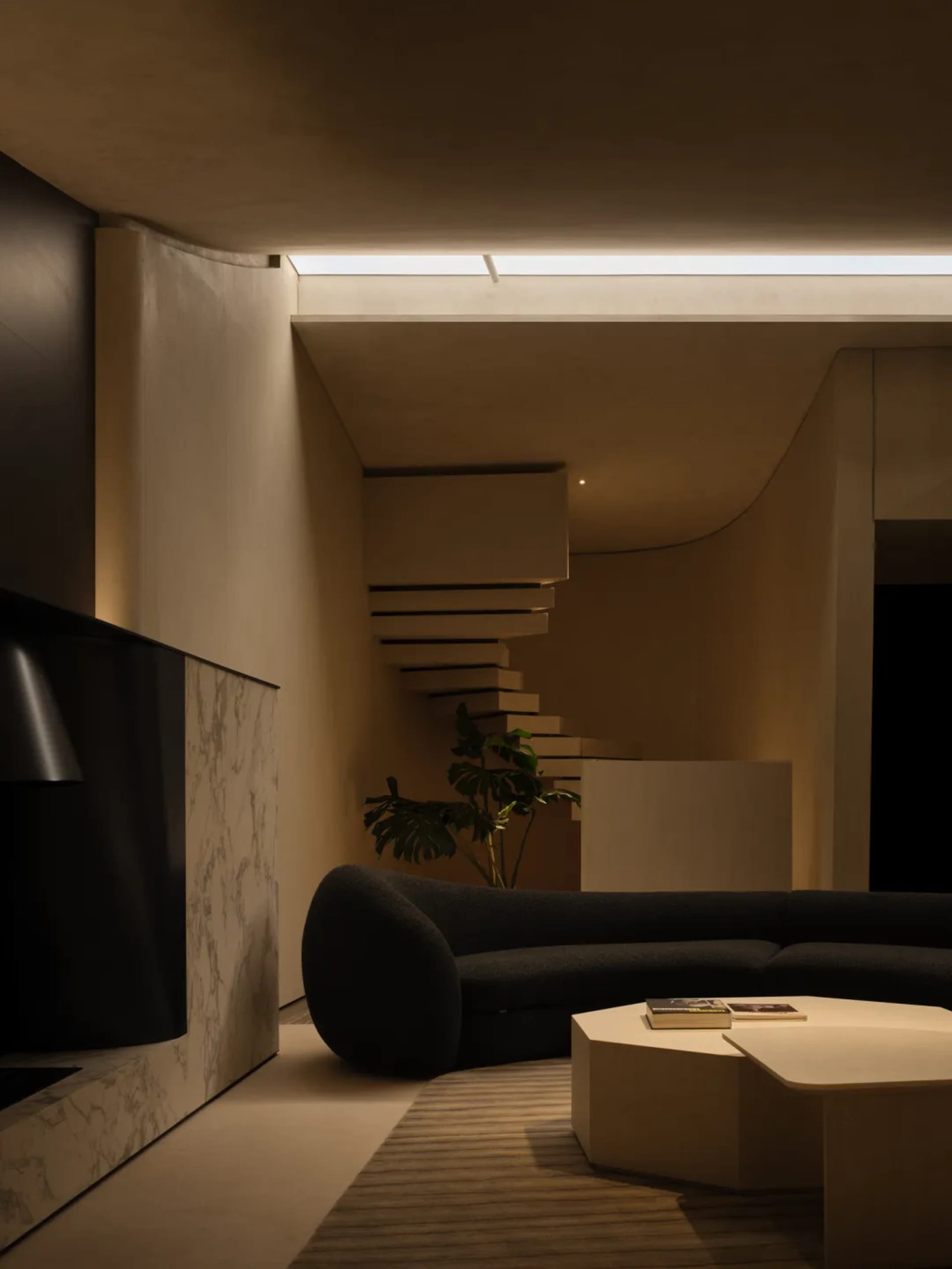 A modern living room with exposed concrete walls, a spiral staircase, and a curved sofa.